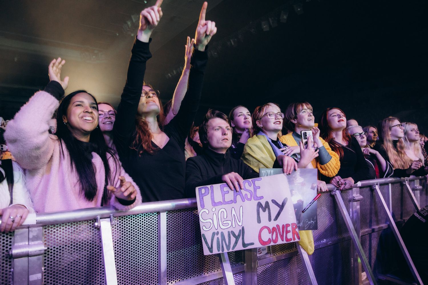 Concert crowd at a live music event cheering and reaching toward the stage with their hands raised in excitement.