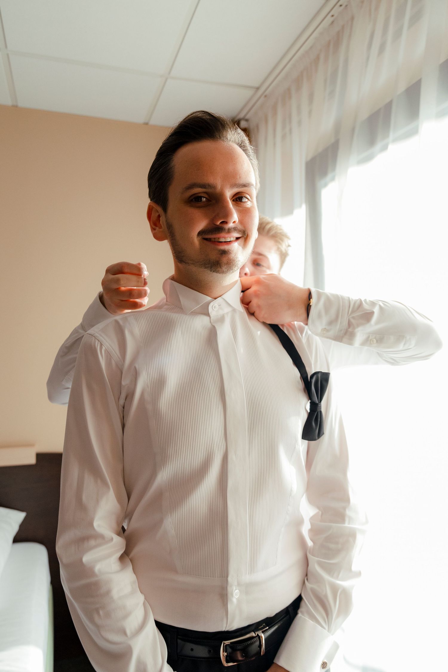 A formal preparation scene with white shirt and bowtie adjustments.
