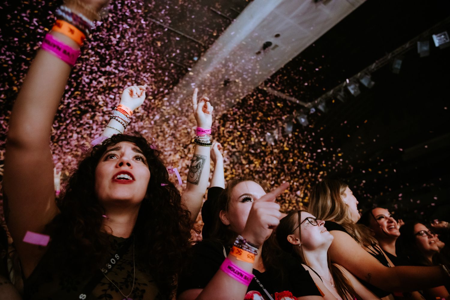 A crowd of concert-goers dance and celebrate under falling pink confetti at a nightclub event.