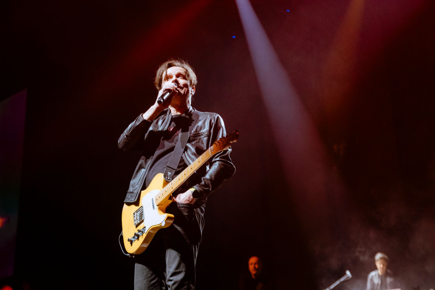 A guitarist performs on stage with dramatic red lighting during a live concert performance.