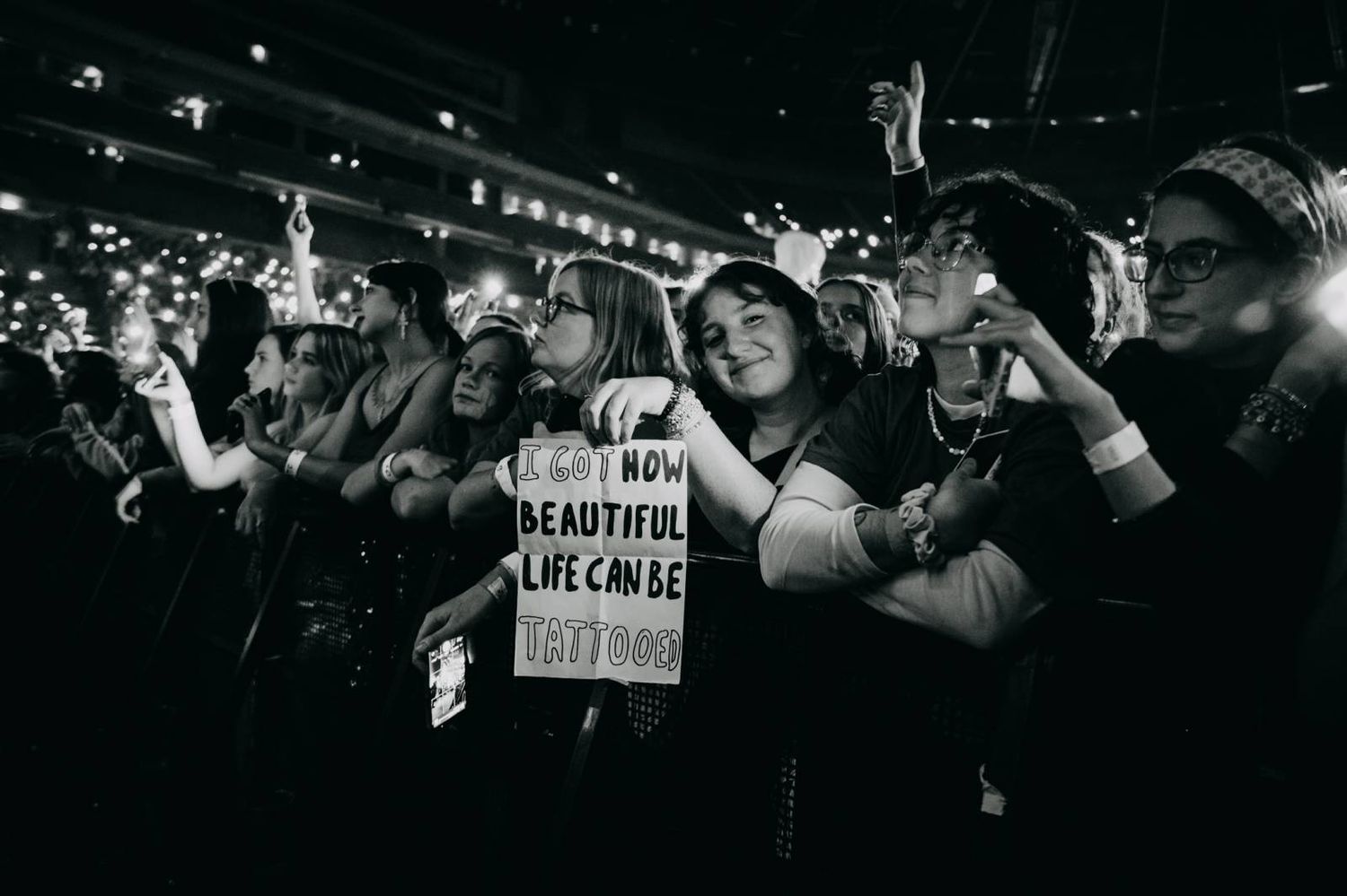 Enthusiastic concert audience holding signs and reaching out in dark venue with dramatic lighting.