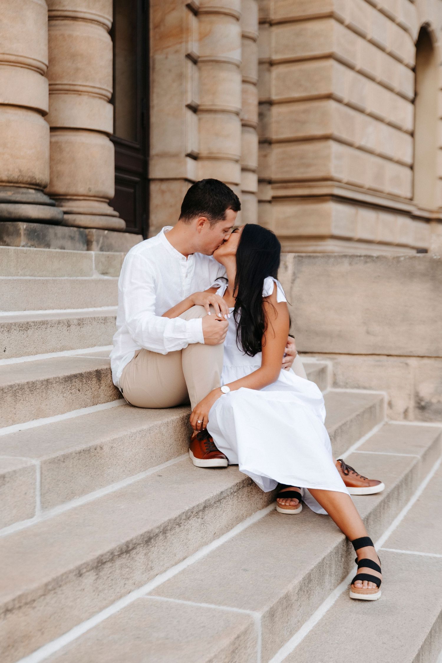 Couple in white and beige outfits sharing tender moments on grand stone steps.