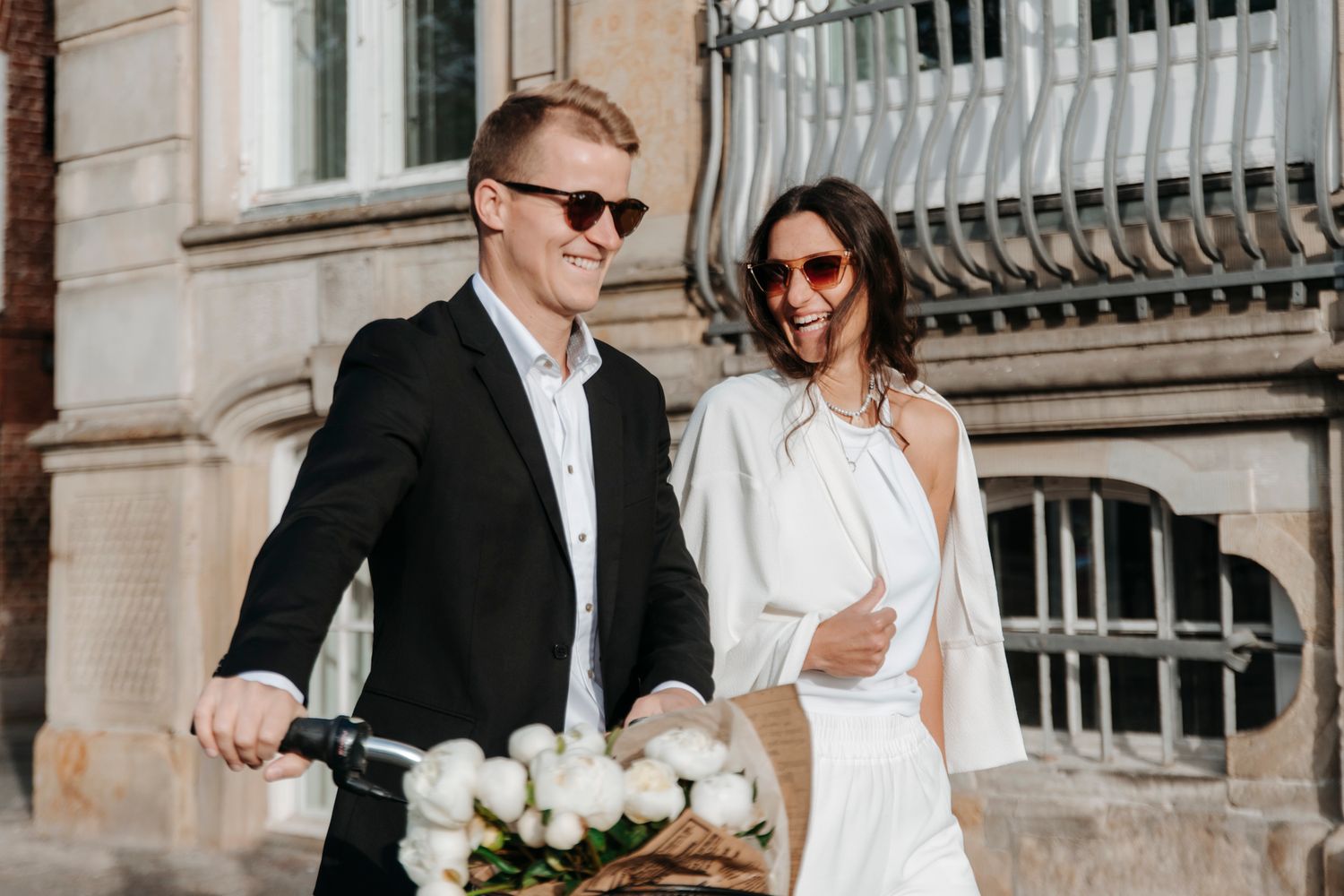 A couple in formal attire walks along a historic stone building exterior.