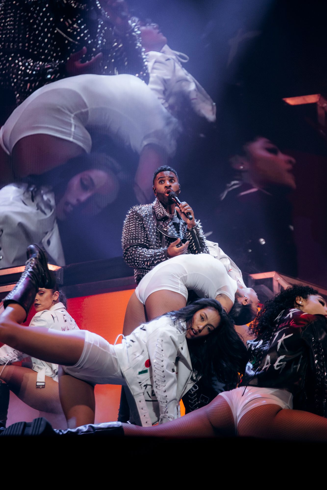 Performance scene with dancers in white outfits on stage with dramatic purple and blue lighting effects.