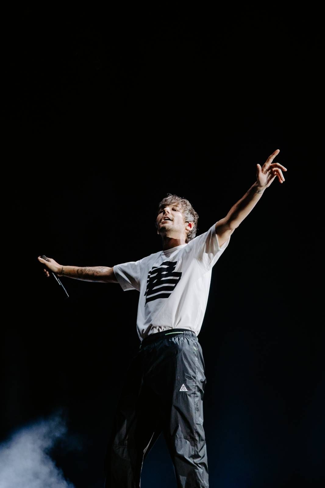 Performer in white shirt and cargo pants striking dynamic pose on smoky stage.