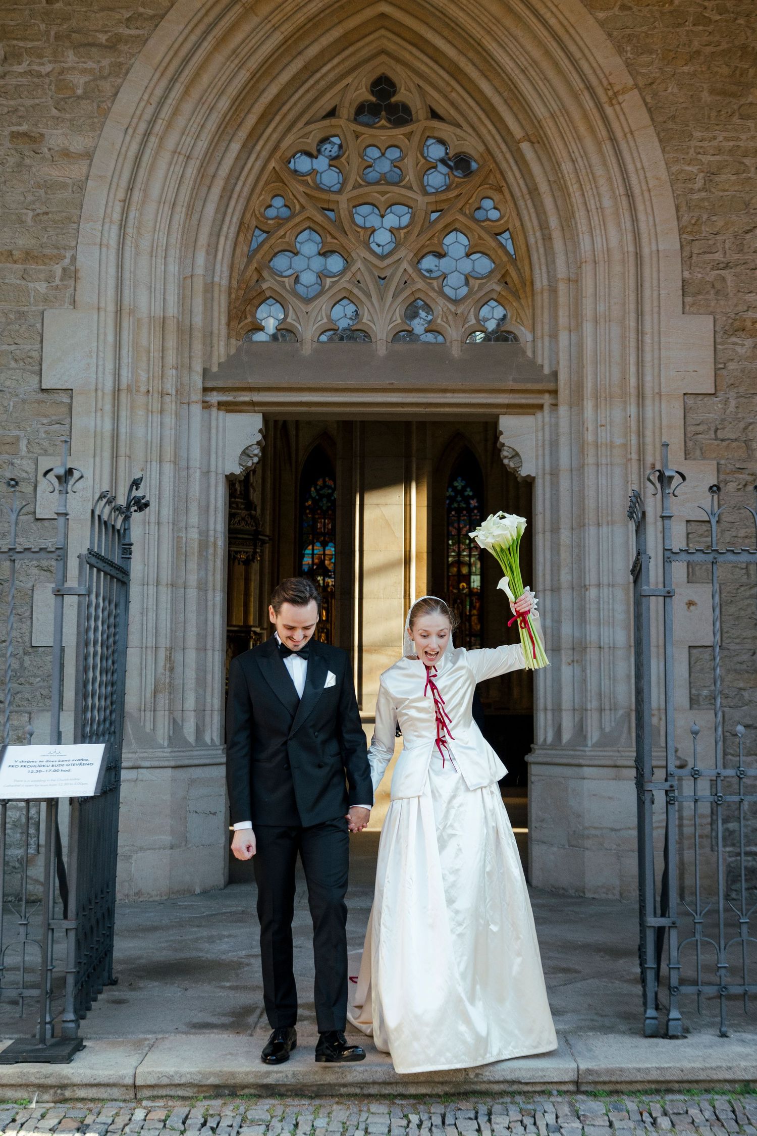A wedding couple poses under Gothic stone archways with ornate architectural details.