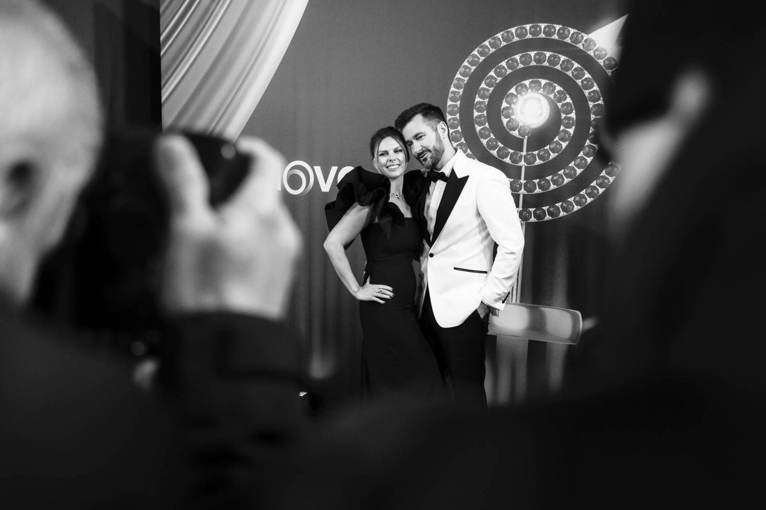 Black and white photo of a glamorous red carpet moment with ornate backdrop at an awards ceremony.