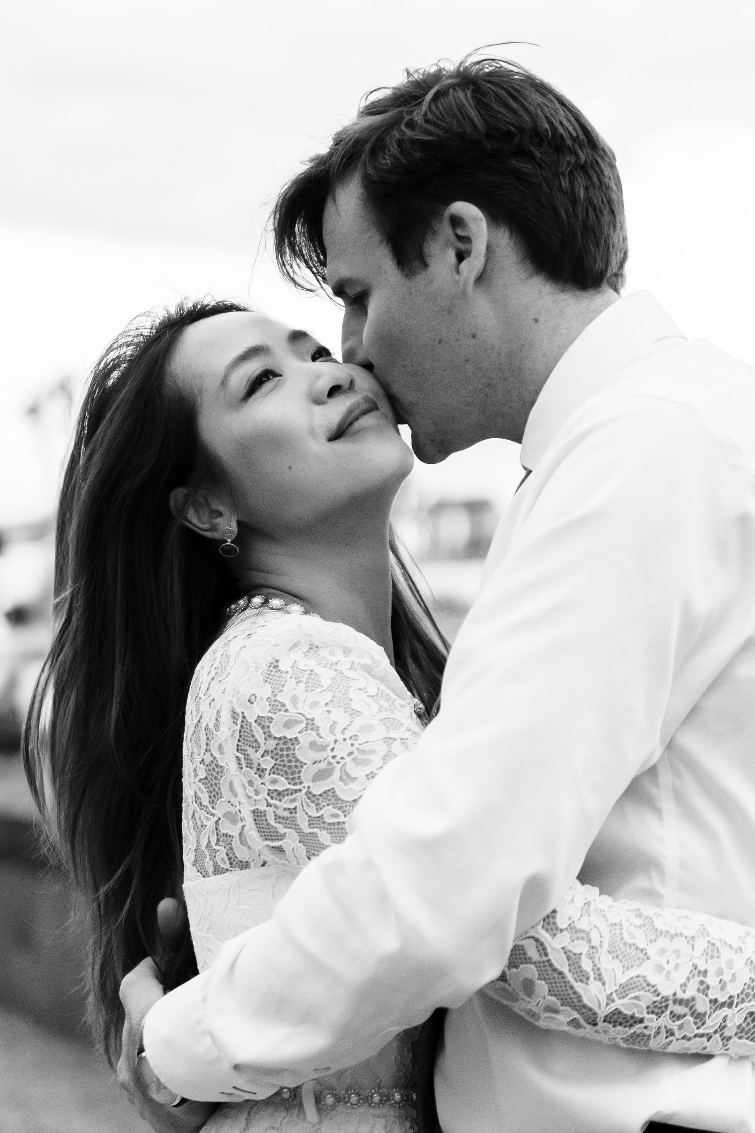 Black and white intimate portrait of couple in romantic embrace wearing white formal attire.