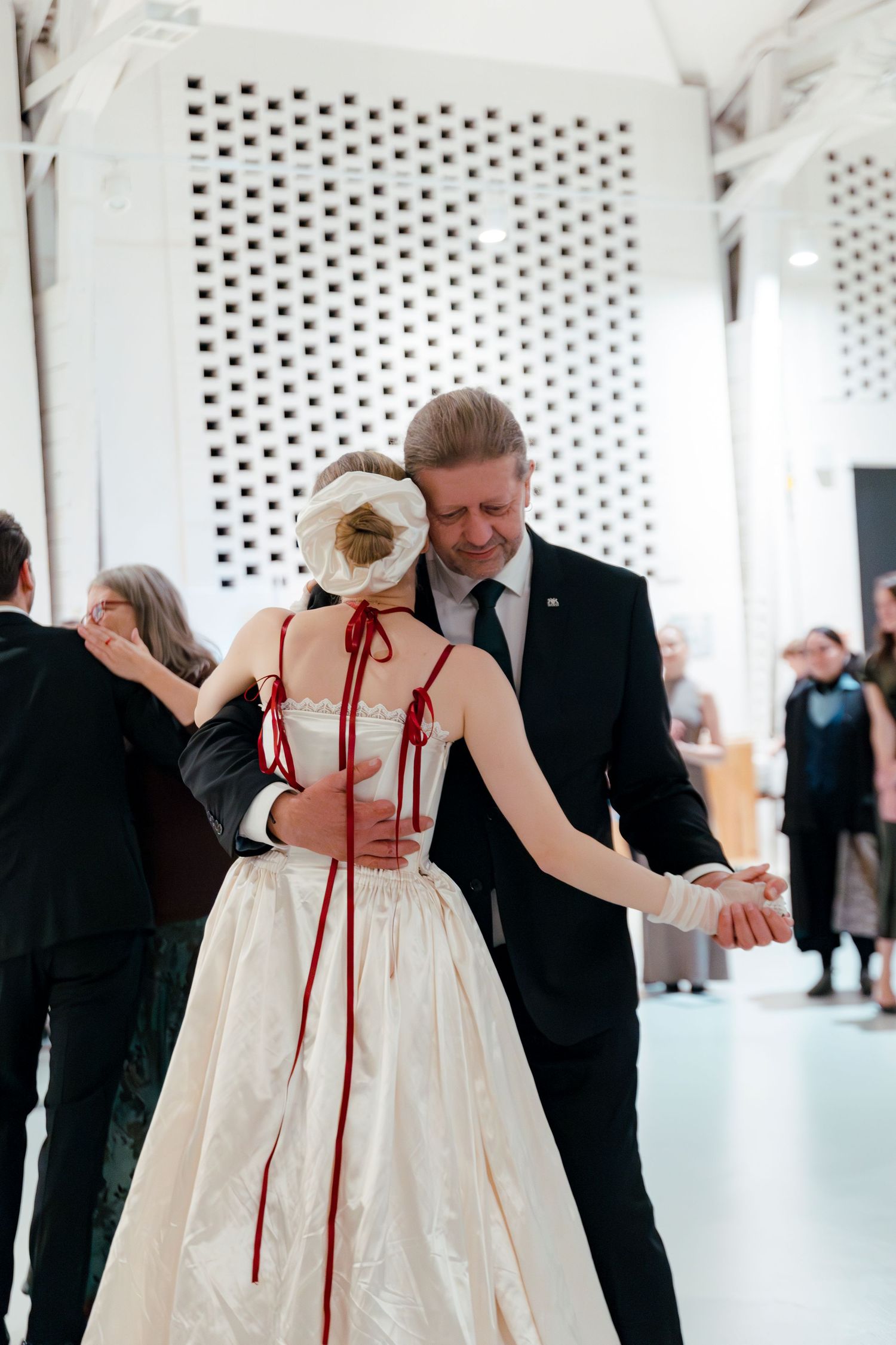 A couple shares a dance, with the dress featuring distinctive red ribbon ties down the back.
