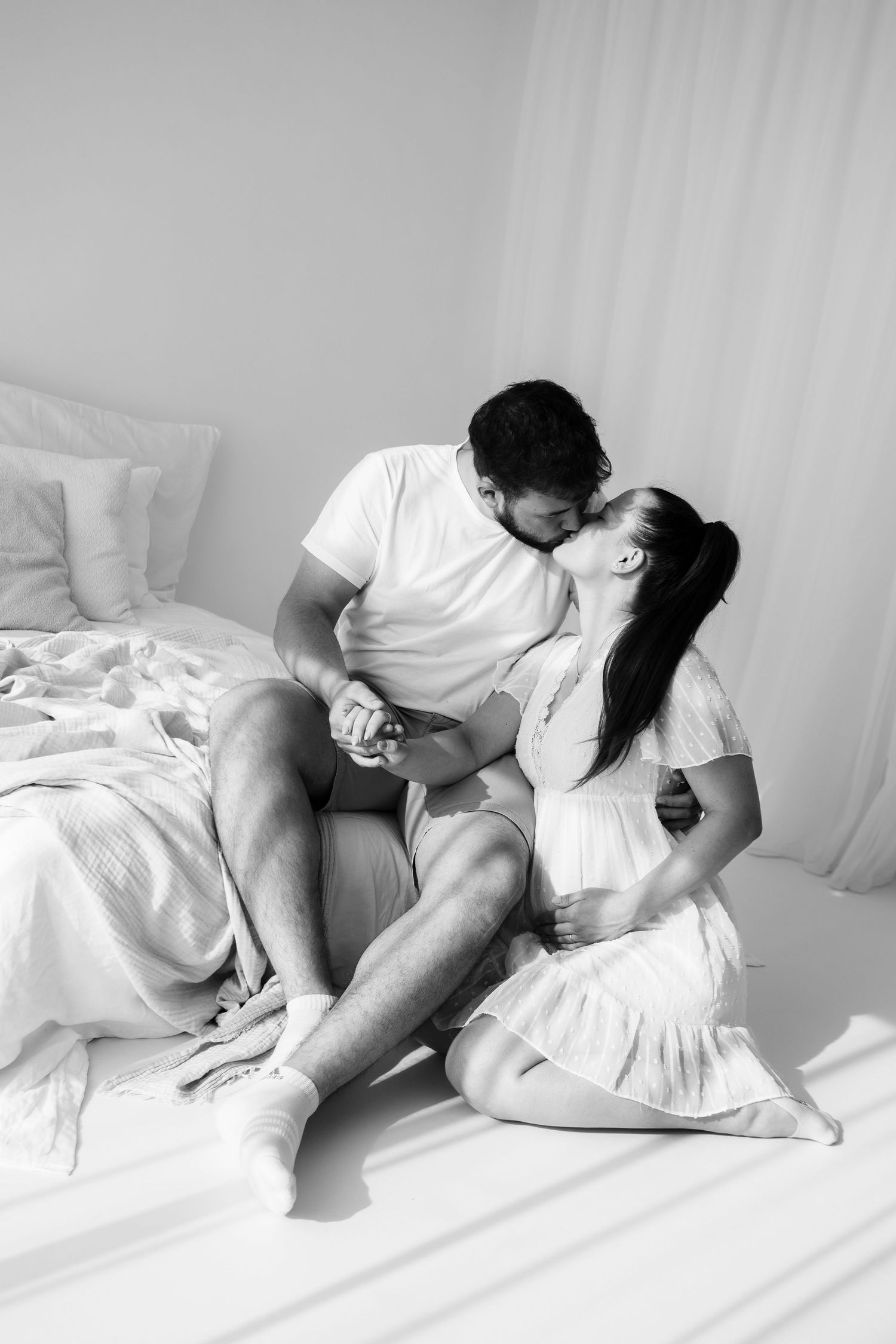 Intimate black and white photo of a couple sharing a tender moment on white bedding.