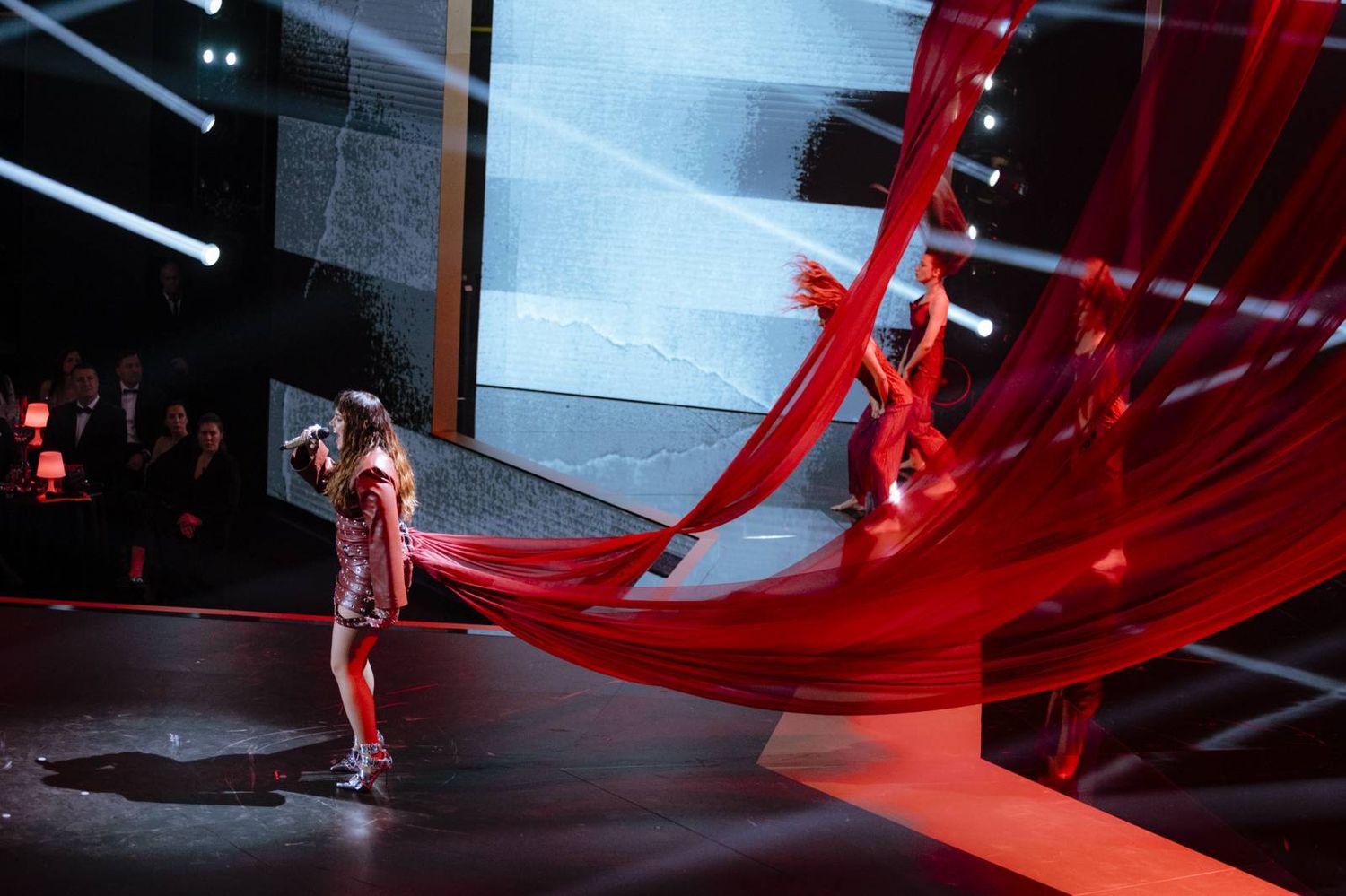 Dramatic stage performance with flowing red fabric and dramatic lighting effects during a live show.