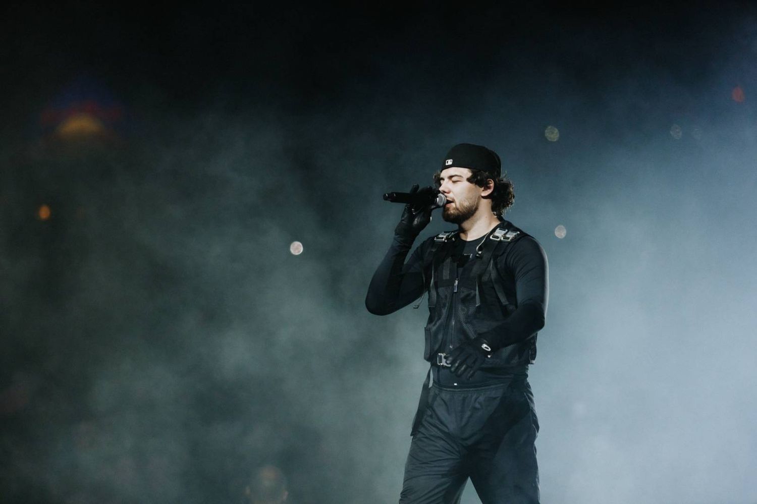 A performer on stage in dark lighting with atmospheric fog effects during a concert performance.