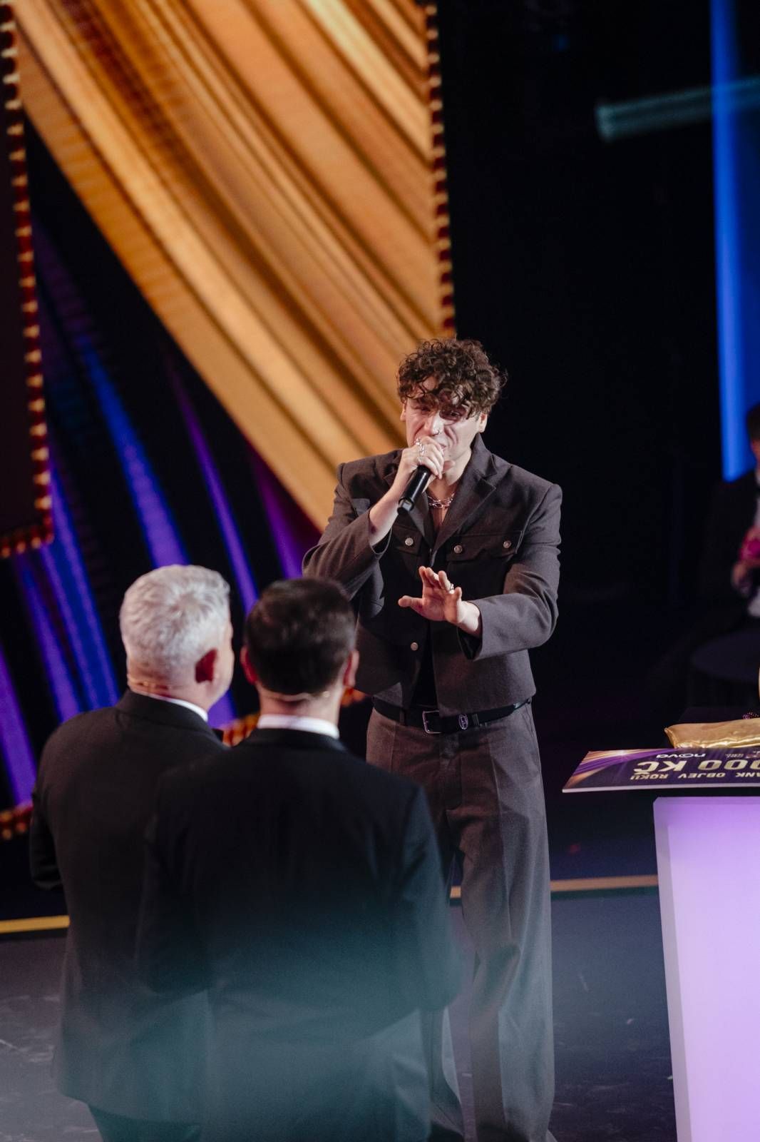 Performers on stage at an awards ceremony with dramatic lighting and gold curtains in the background.