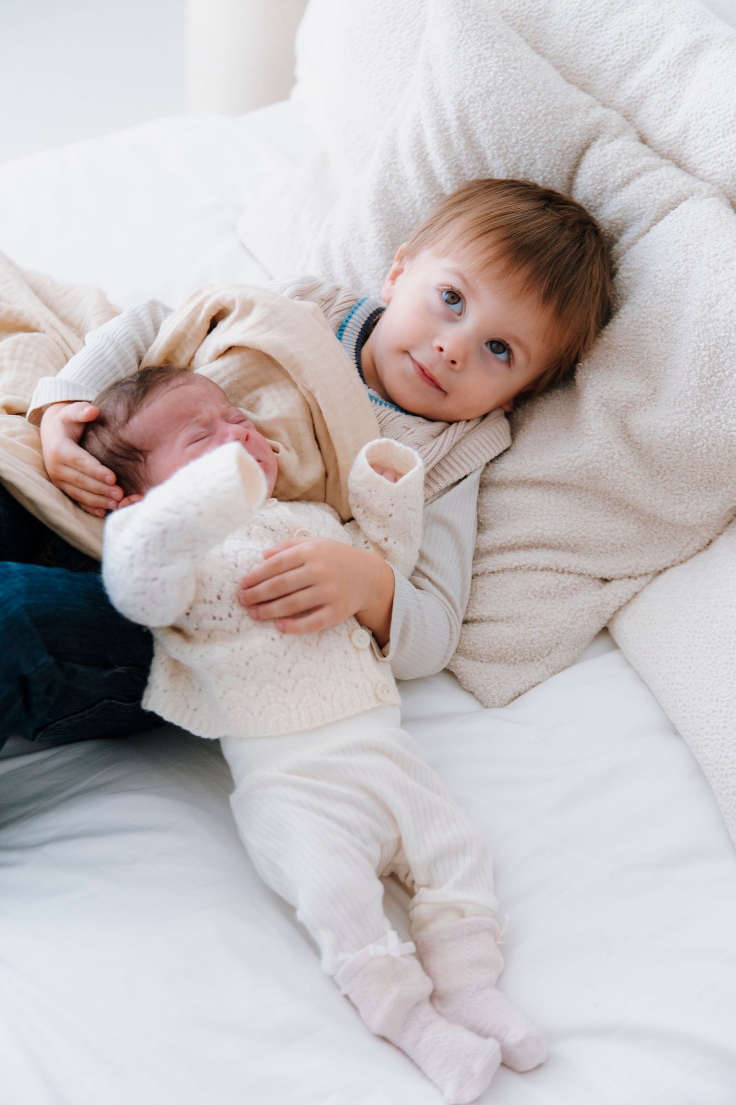Child in white clothing lying on soft white bedding.