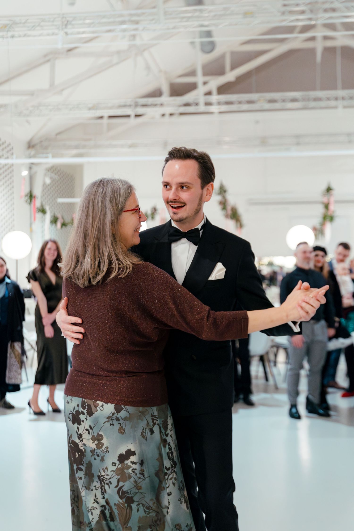 Couples dance together in a bright indoor venue with white walls and natural lighting.