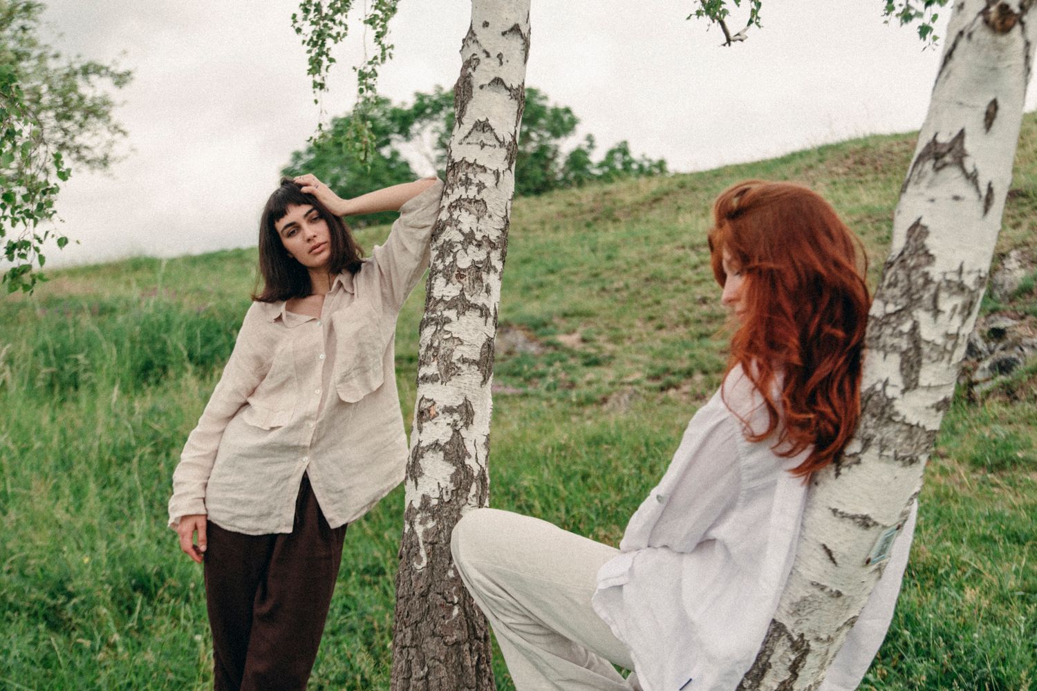 Figure in white clothing posing artistically near birch trees in natural setting.