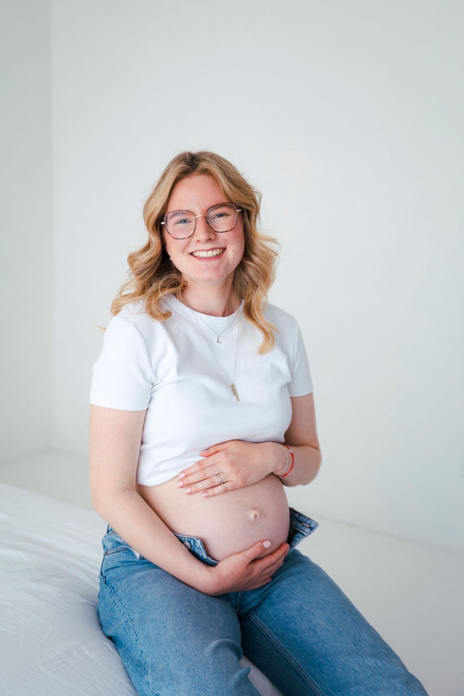Maternity portrait of woman in white shirt and jeans against white background.