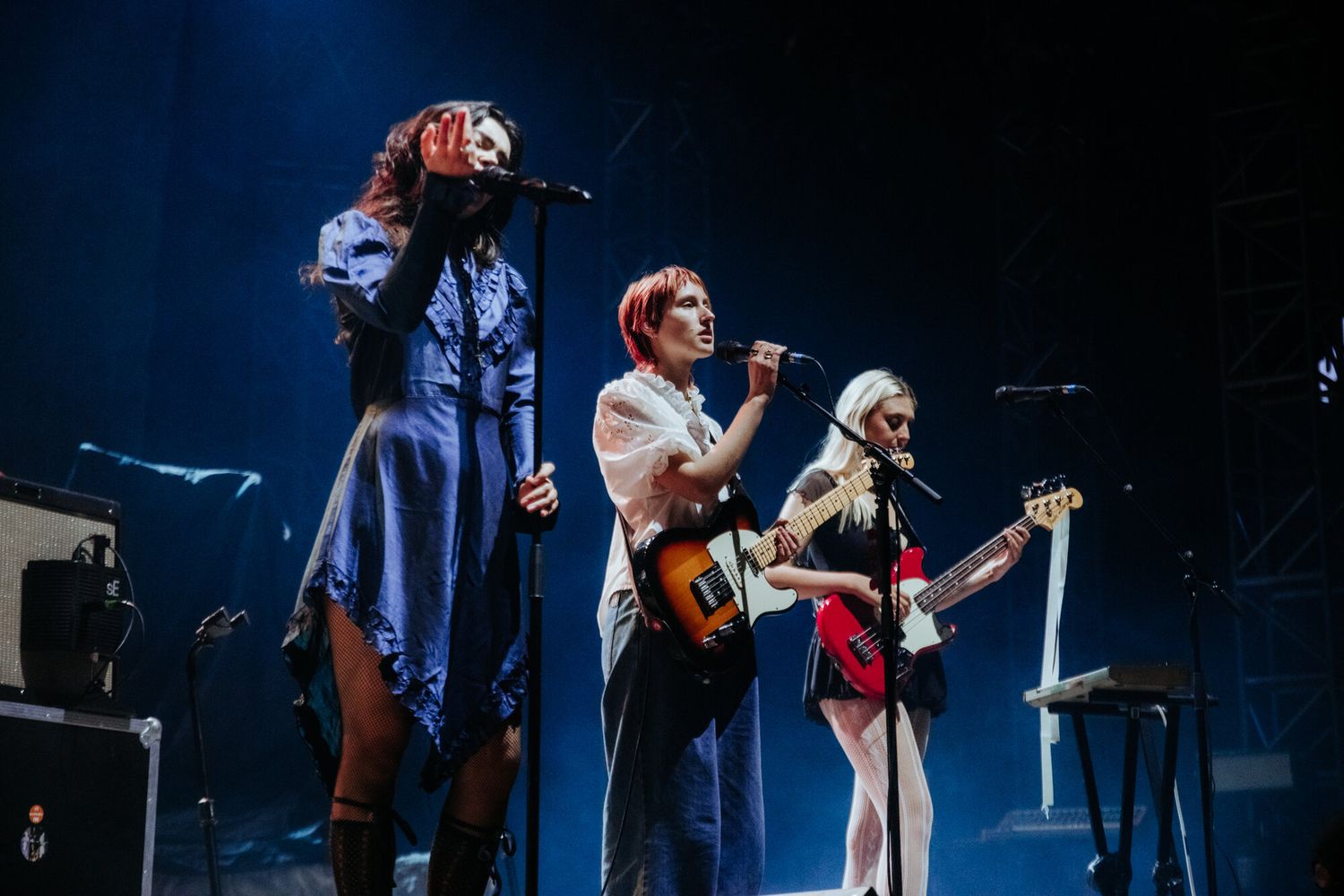 Musicians perform on a dimly lit stage with guitars and instruments during a live concert performance.