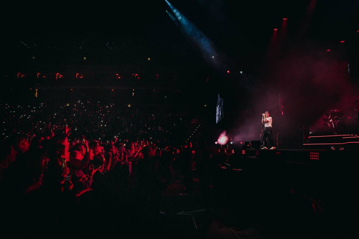 Concert crowd silhouettes in a dark arena with red lighting and stage illumination in the background.