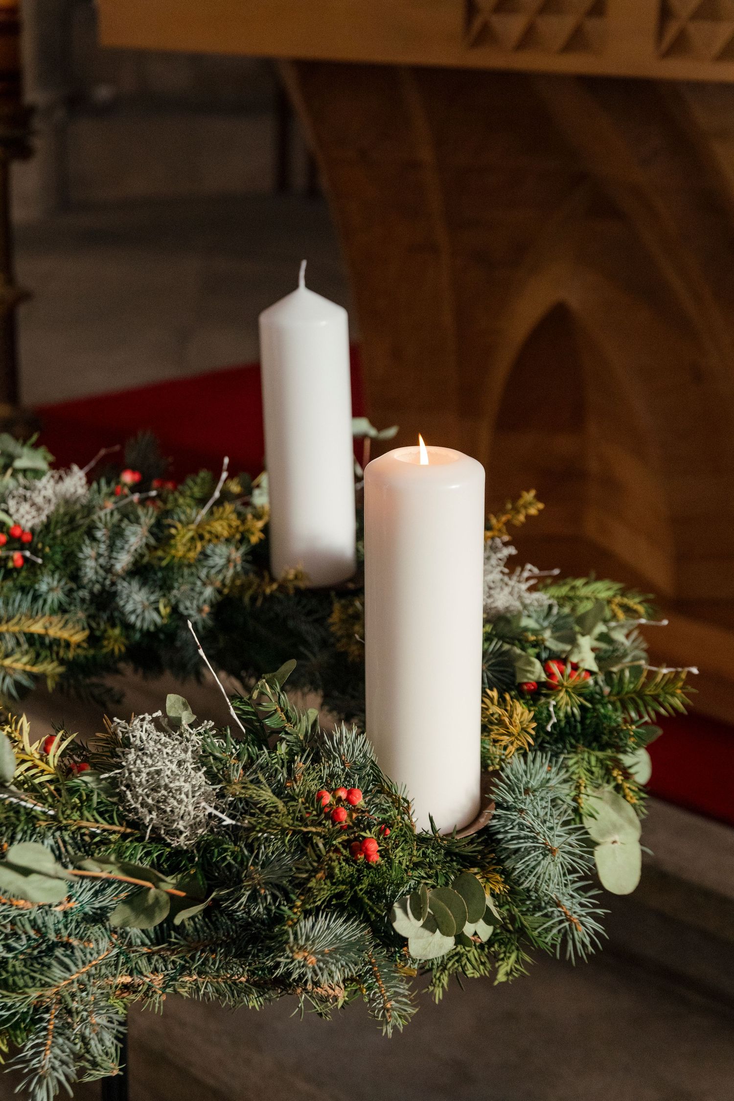 White pillar candles nestled in a festive evergreen garland with red berries and winter foliage.