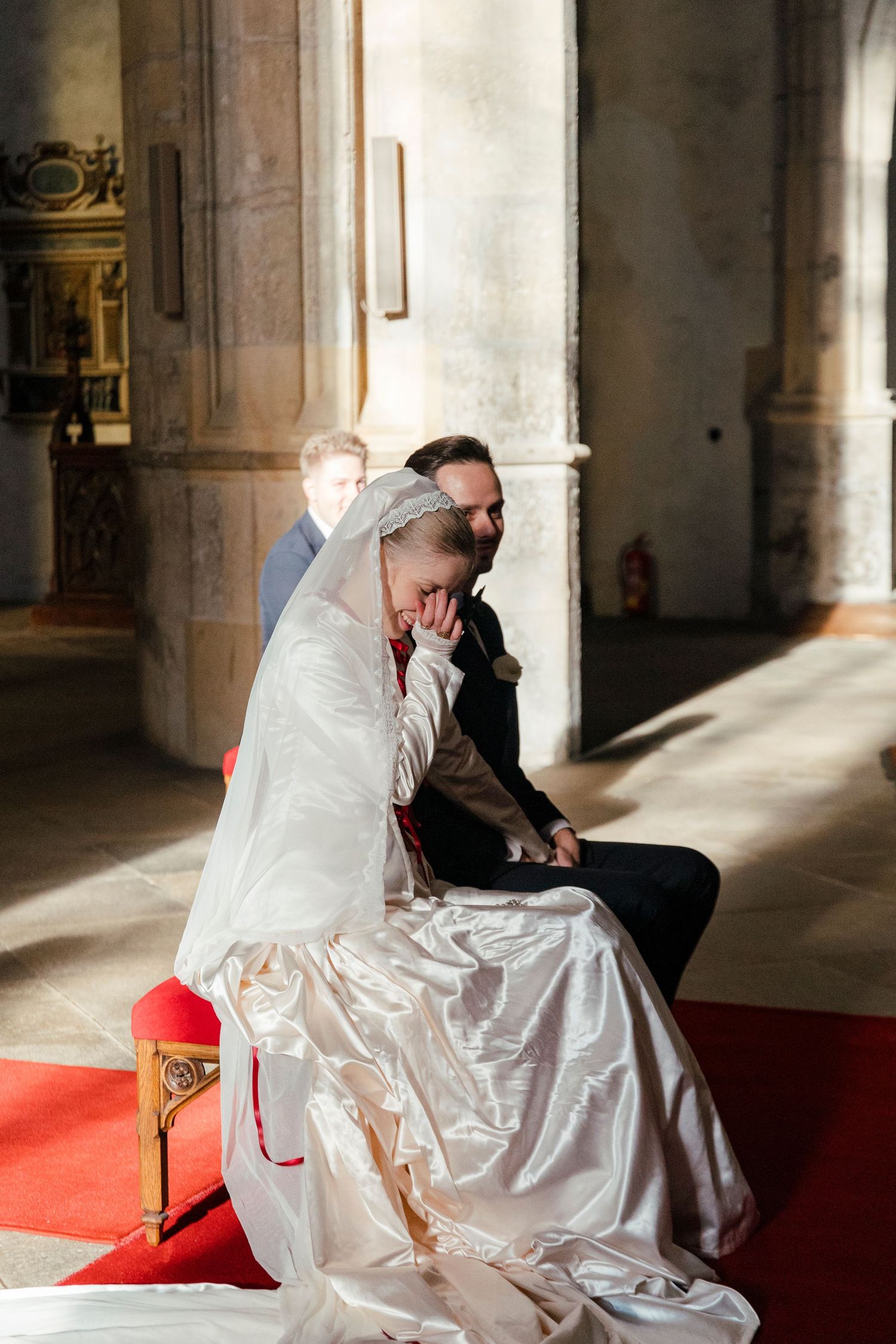 A couple sharing an intimate moment on red cushions in a sunlit church interior.