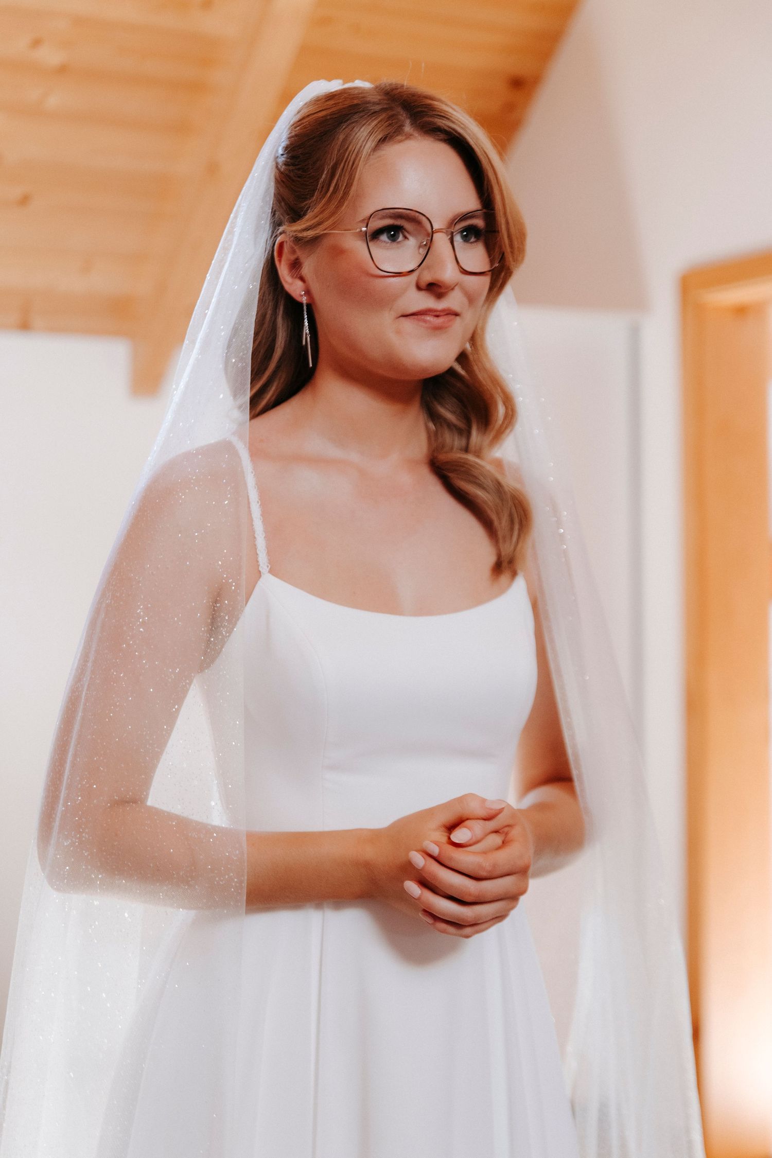 Bride in a simple white wedding dress with flowing veil poses in natural light.