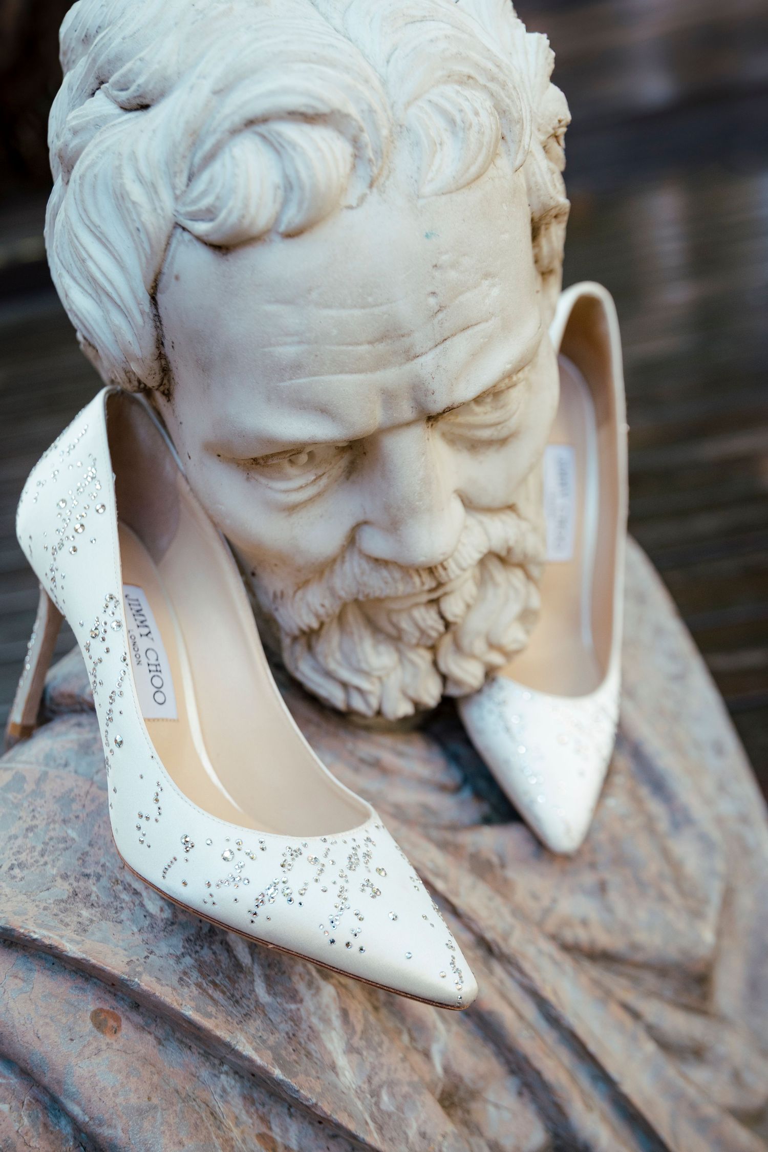 White bridal shoes artistically placed on classical stone bust sculpture.