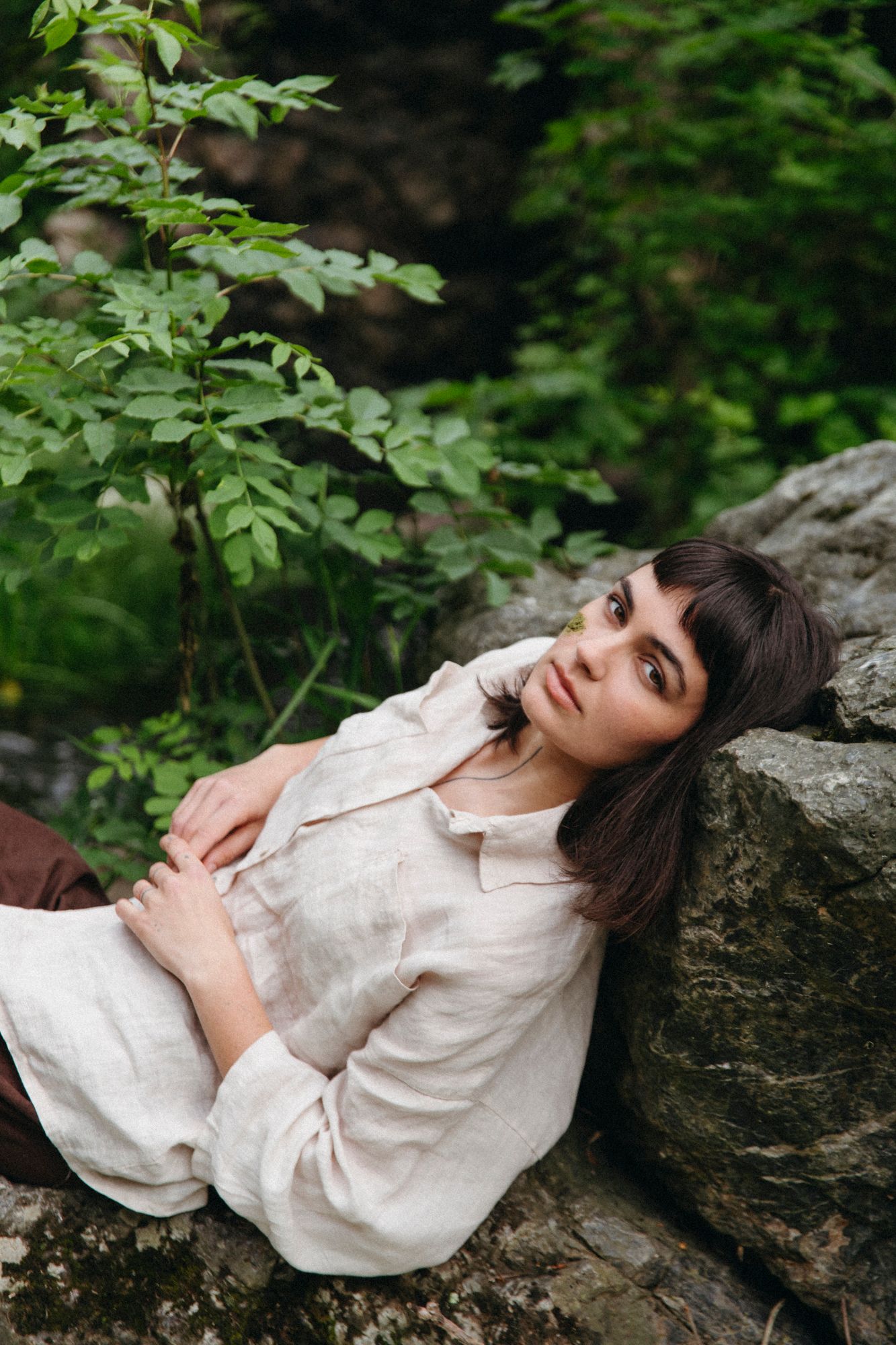 Person in white shirt reclining on rocks surrounded by lush green foliage.