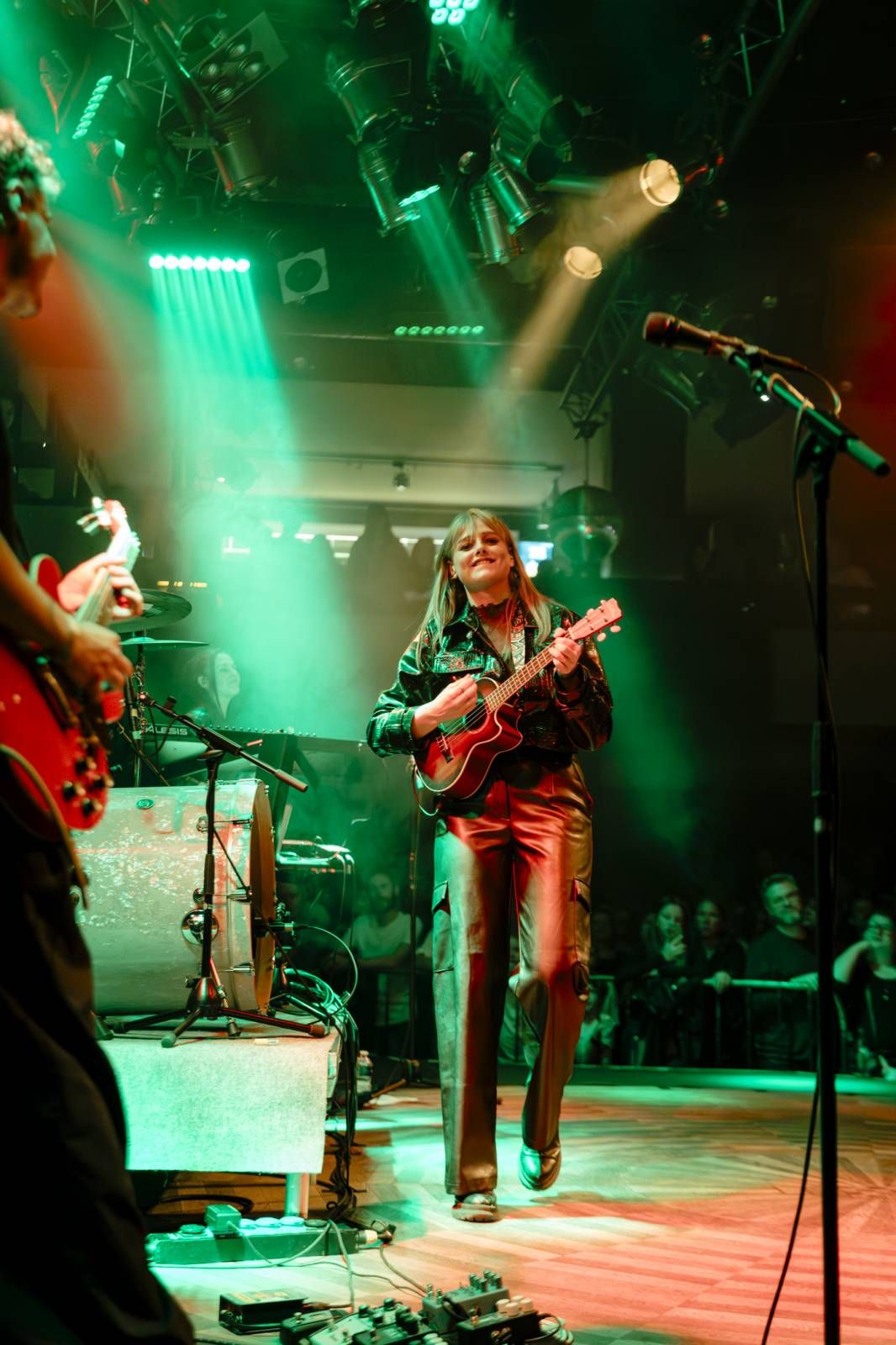 Musicians perform on stage bathed in dramatic green and red lighting during a live concert performance.