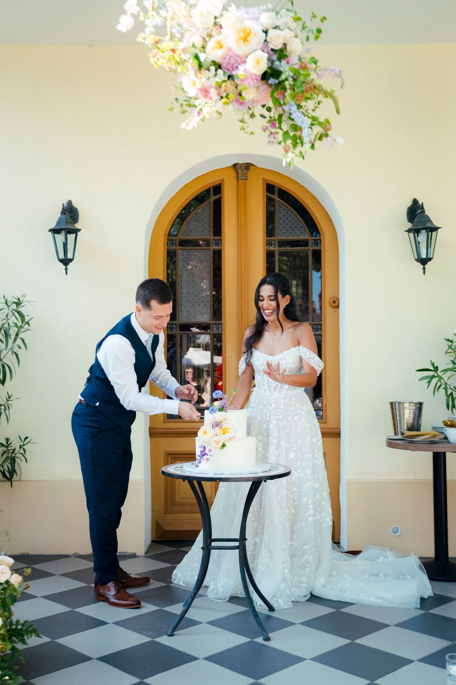 A couple shares cake at their wedding reception on a black and white checkered floor.
