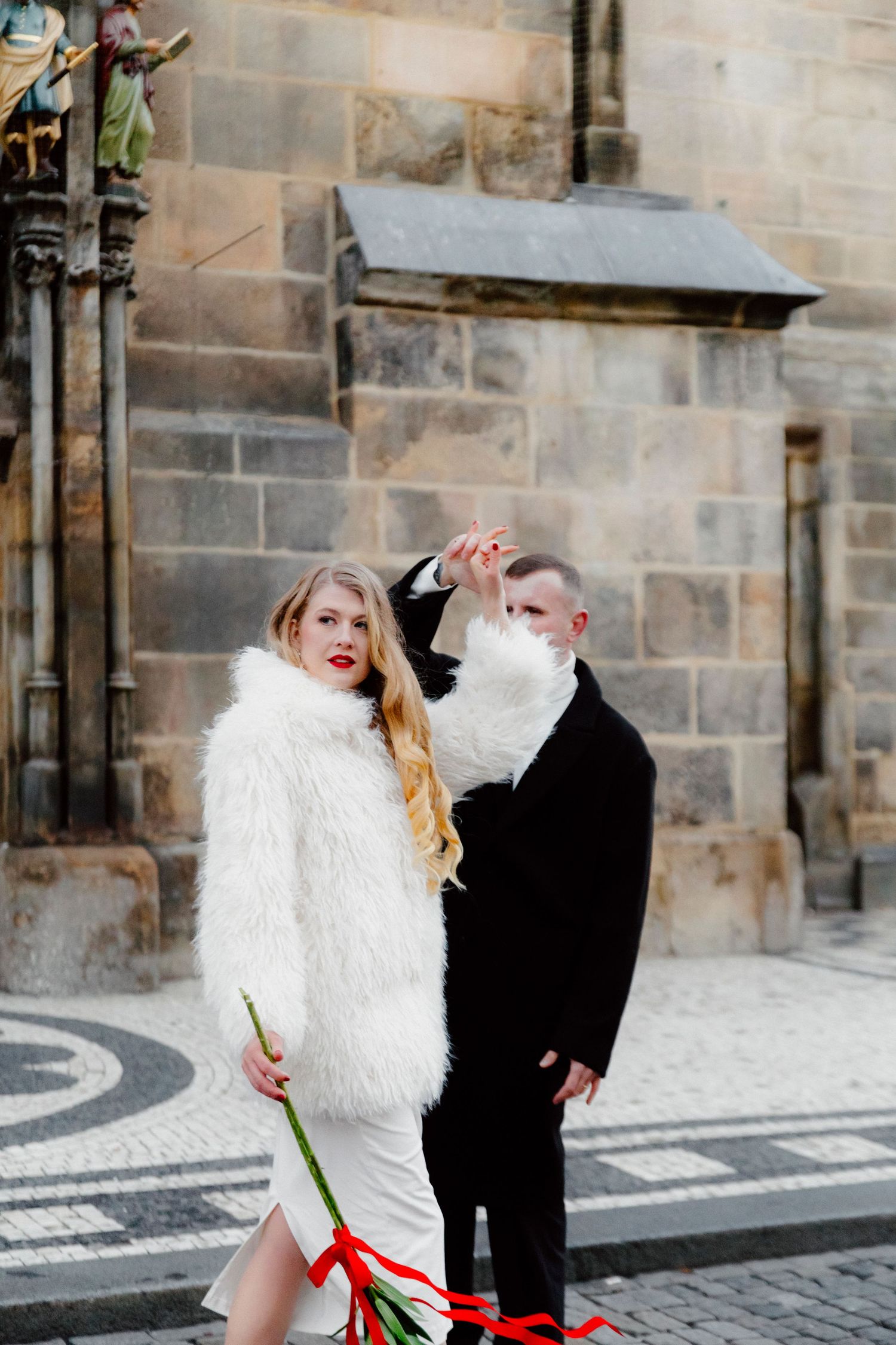 Couple in contrasting black and white outfits posing dramatically against stone architecture.