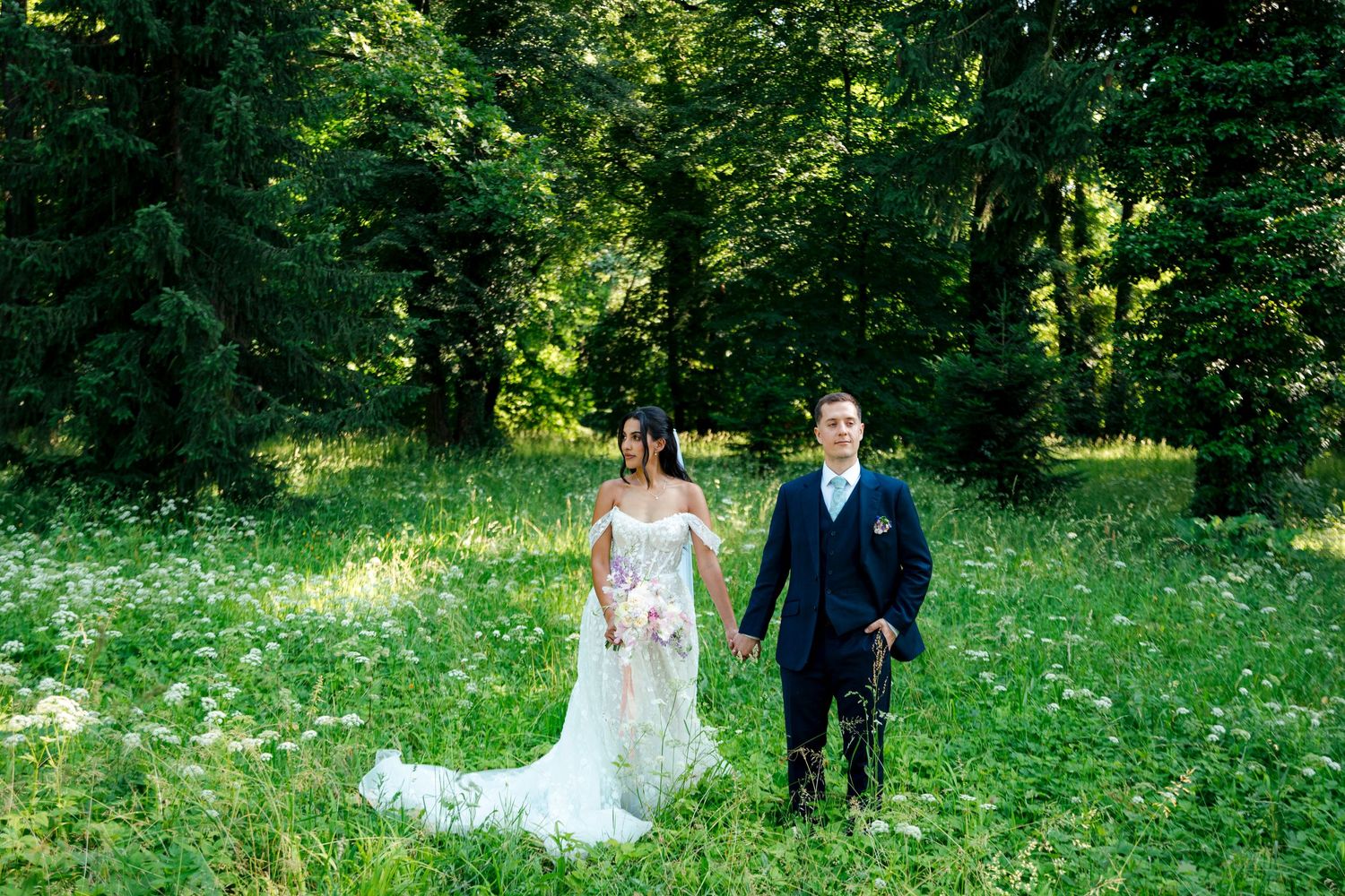 A bride and groom walk through a lush green summer garden.