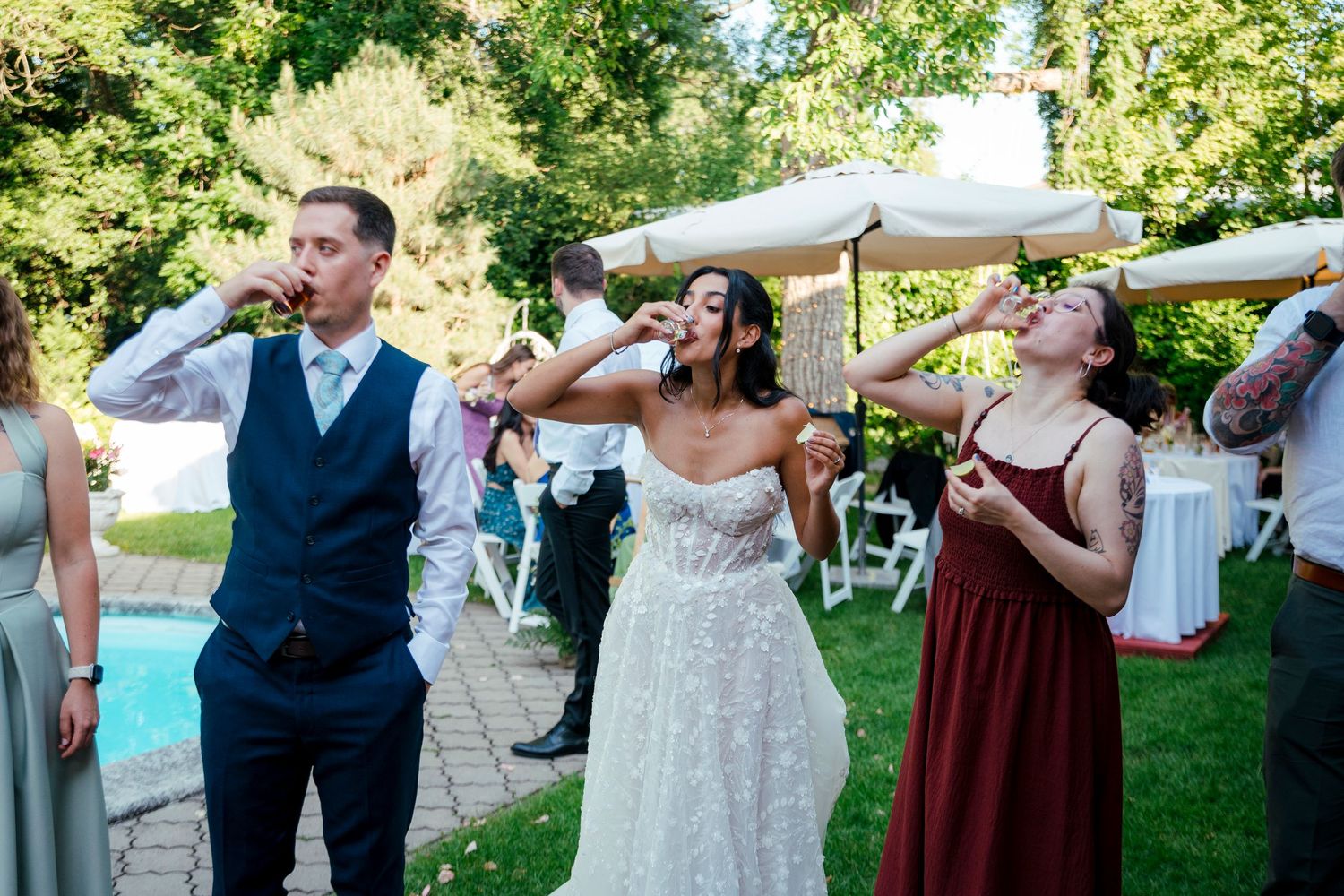 Wedding party guests taking shots together by a pool during an outdoor celebration.