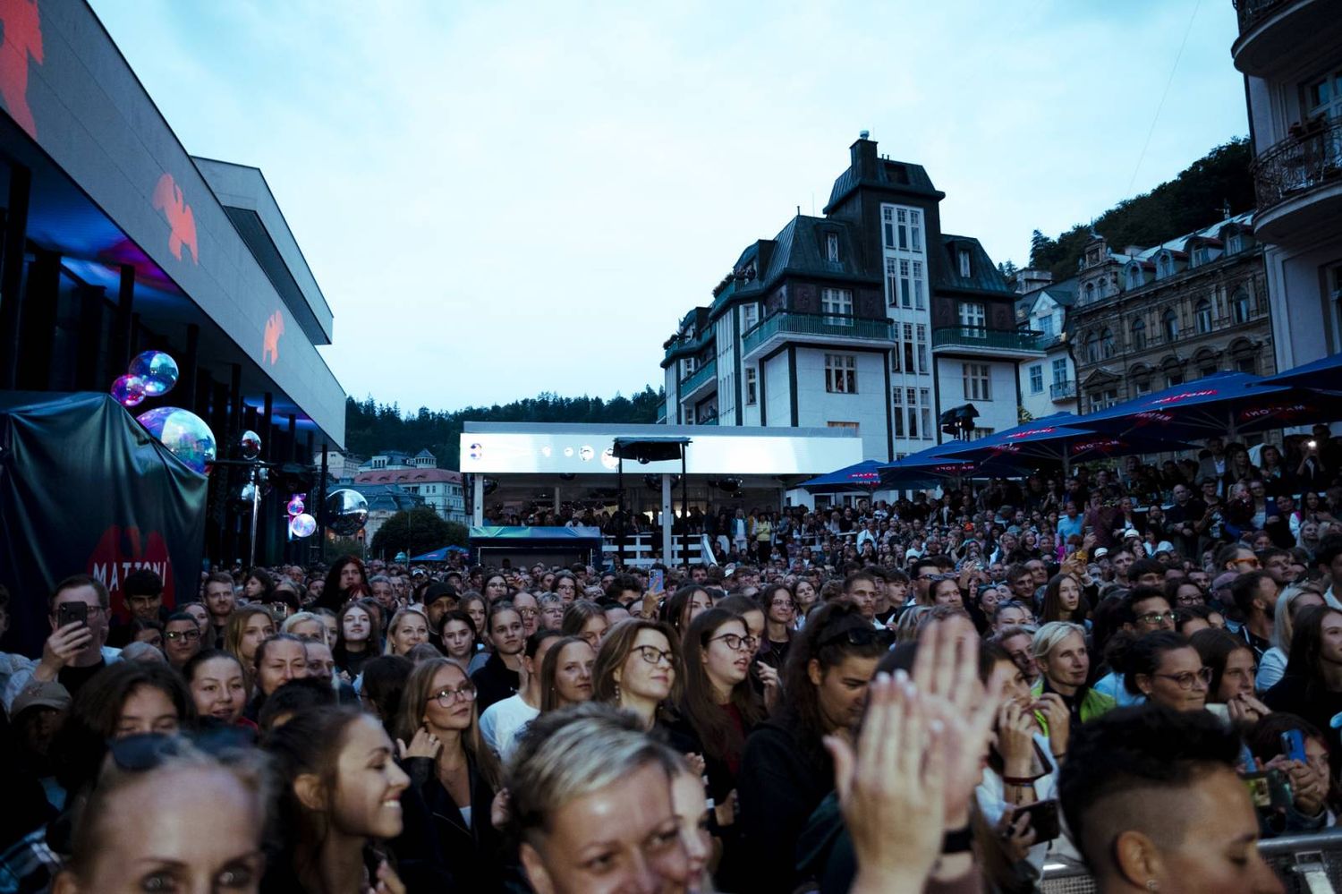 Large crowd gathers on a city street to watch an outdoor event or celebration.