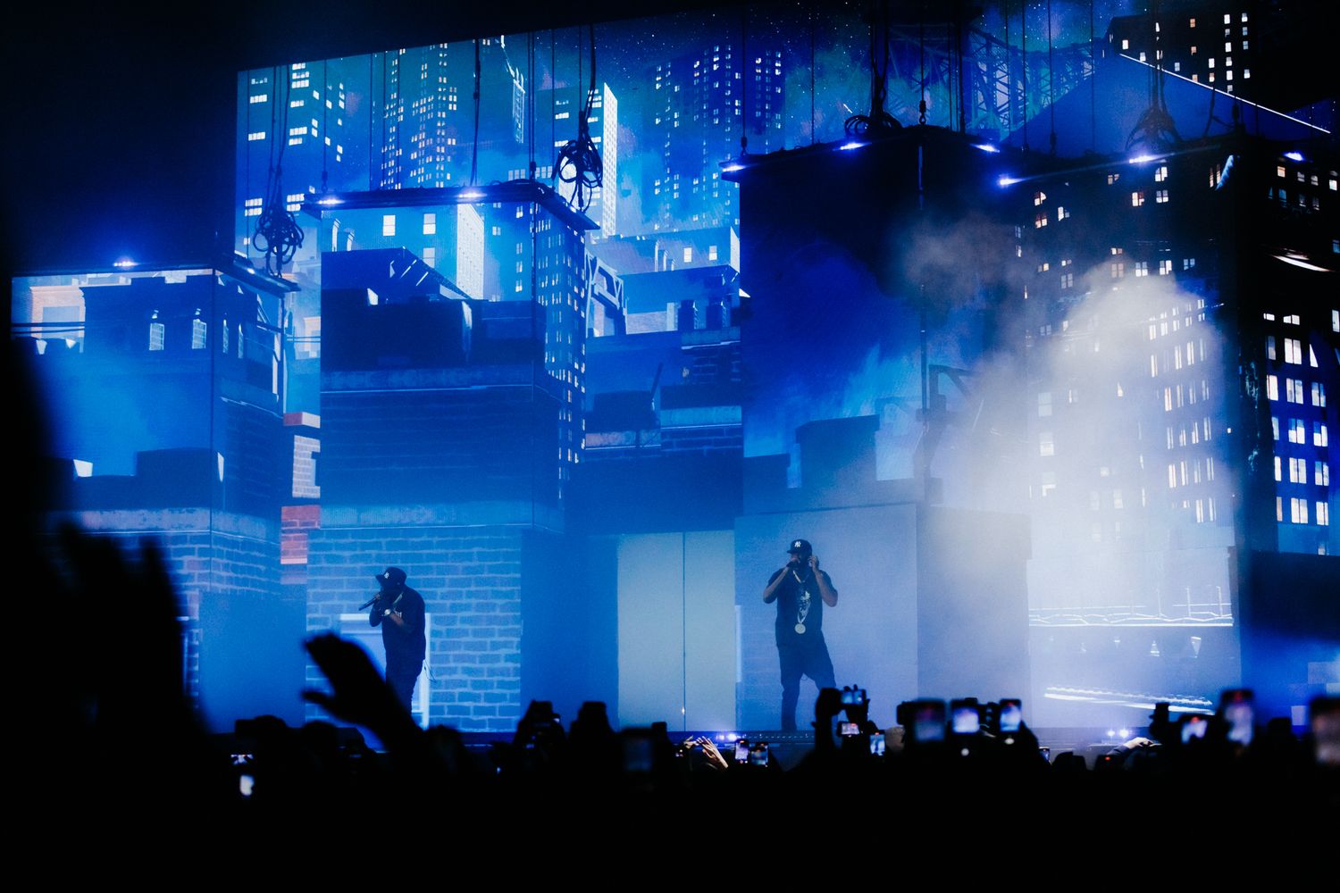 A moody nighttime cityscape bathed in blue light with fog and silhouettes creating a cyberpunk atmosphere.