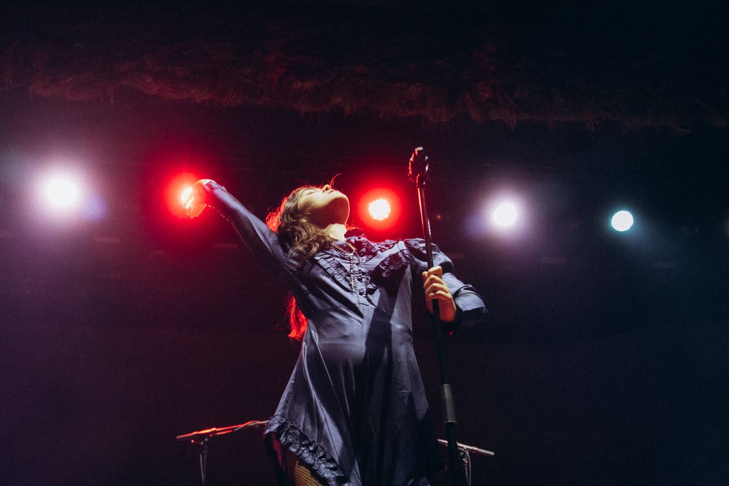 Concert performer on dark stage illuminated by red and white spotlights during dramatic live music performance.