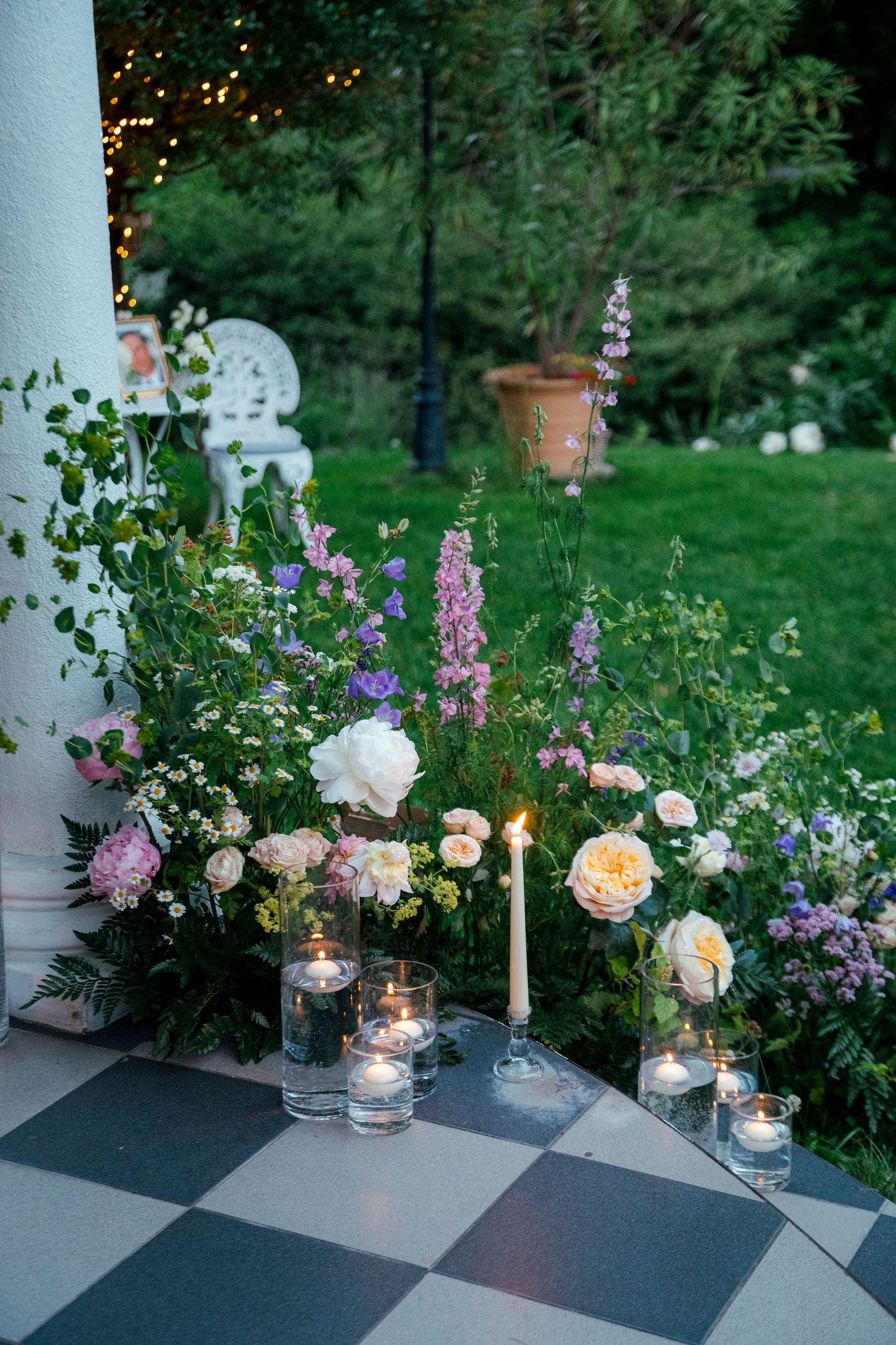 Elegant garden wedding decor with candles, pink roses and purple flowers at dusk.