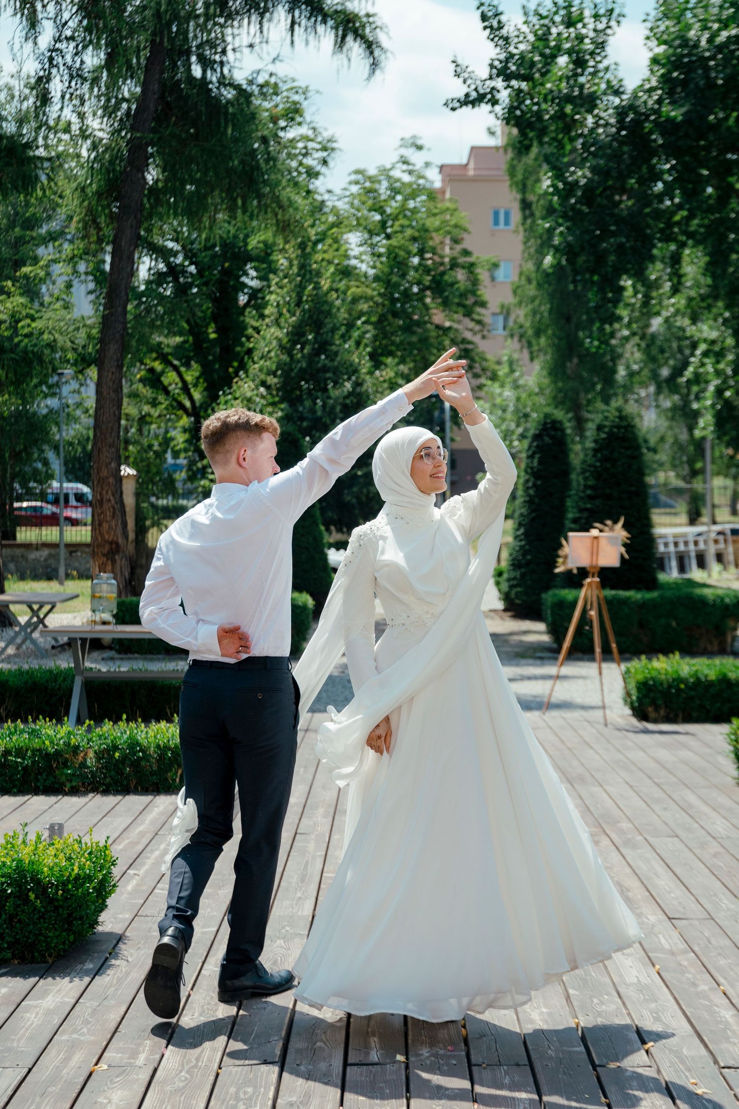 Wedding couple dancing and twirling on an outdoor wooden deck surrounded by trees.