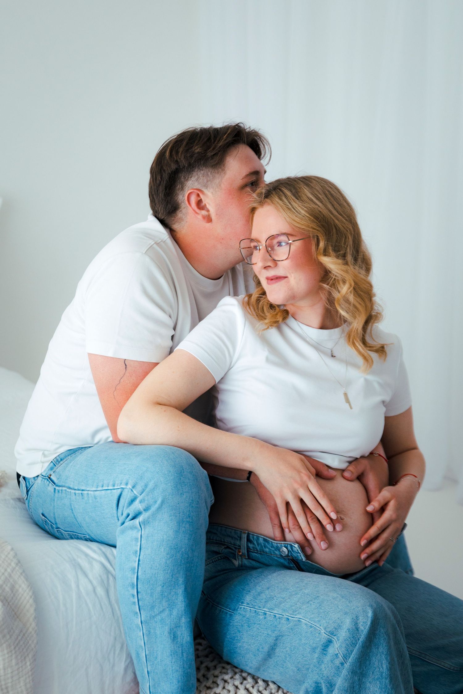 Maternity photo of couple in white shirts and jeans sharing intimate moment.