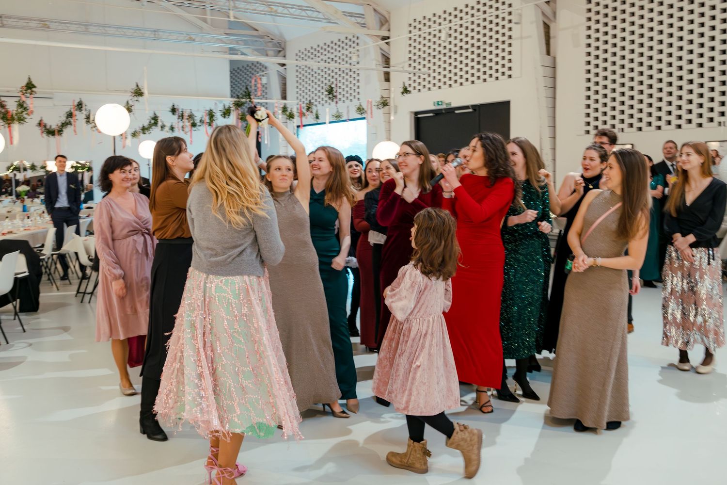 A lively wedding reception with guests dancing in a bright indoor venue.