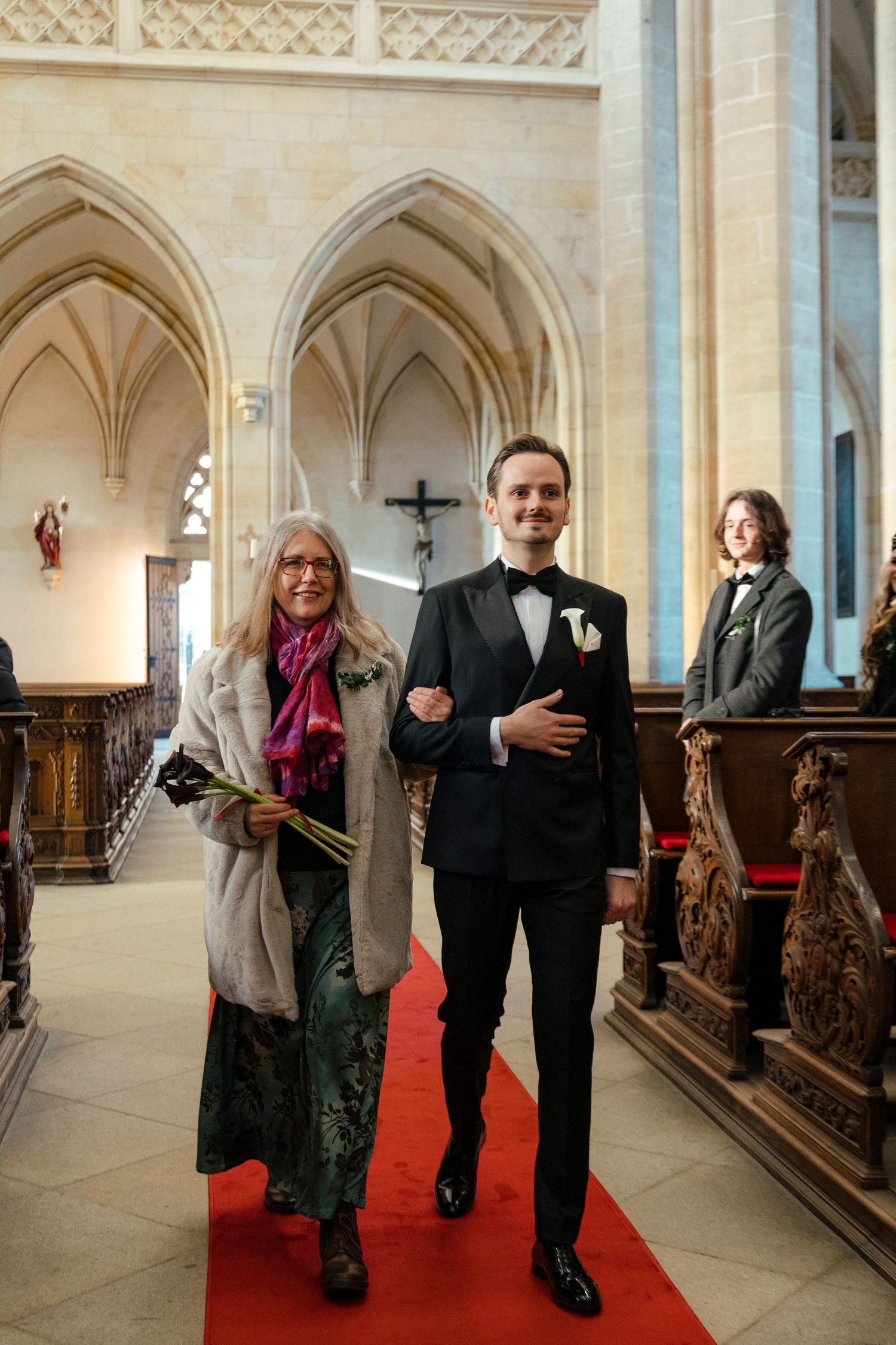Wedding guests walking down a cathedral aisle with gothic architecture and a red carpet.
