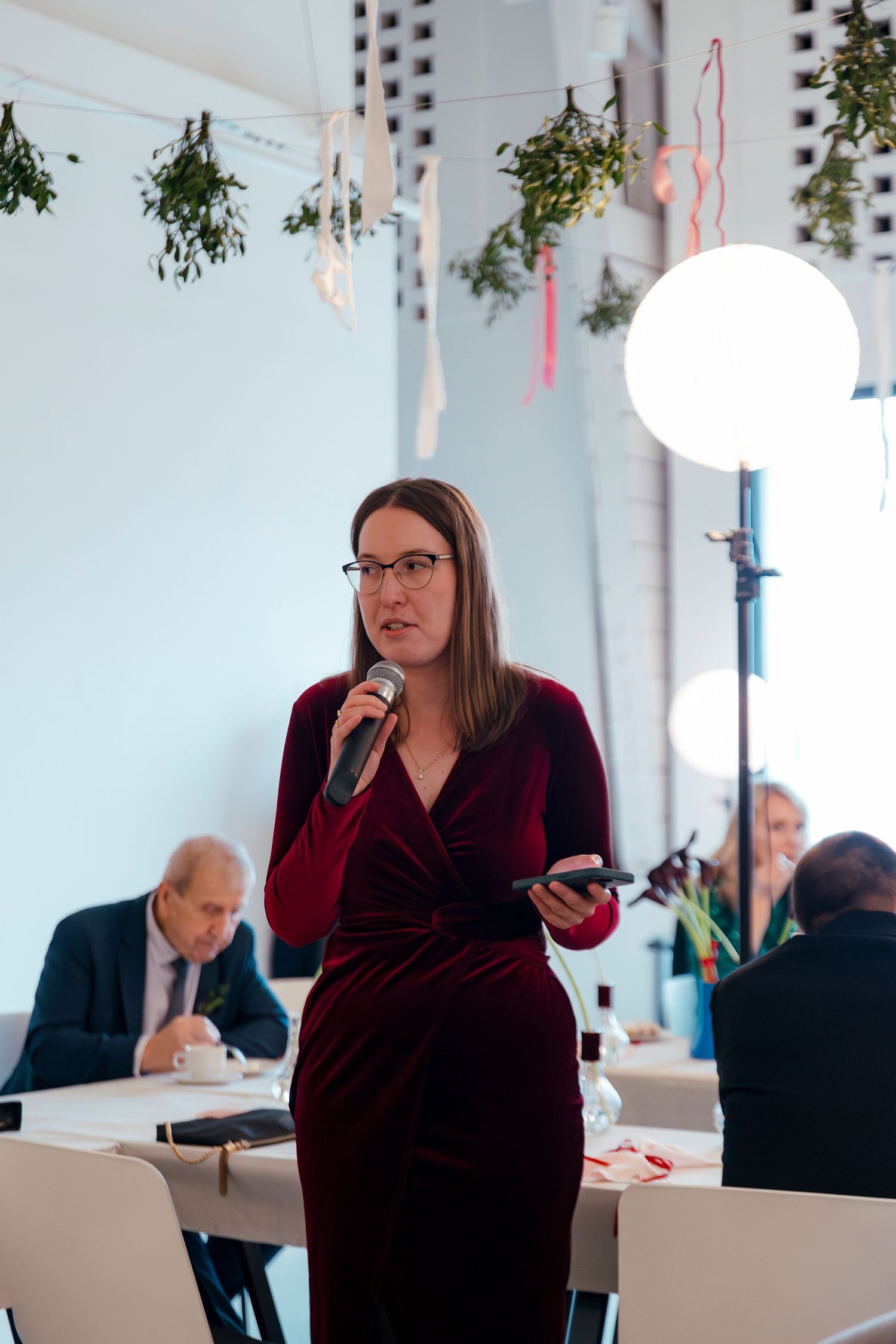 Person in burgundy velvet dress standing in modern office space with hanging decorations.