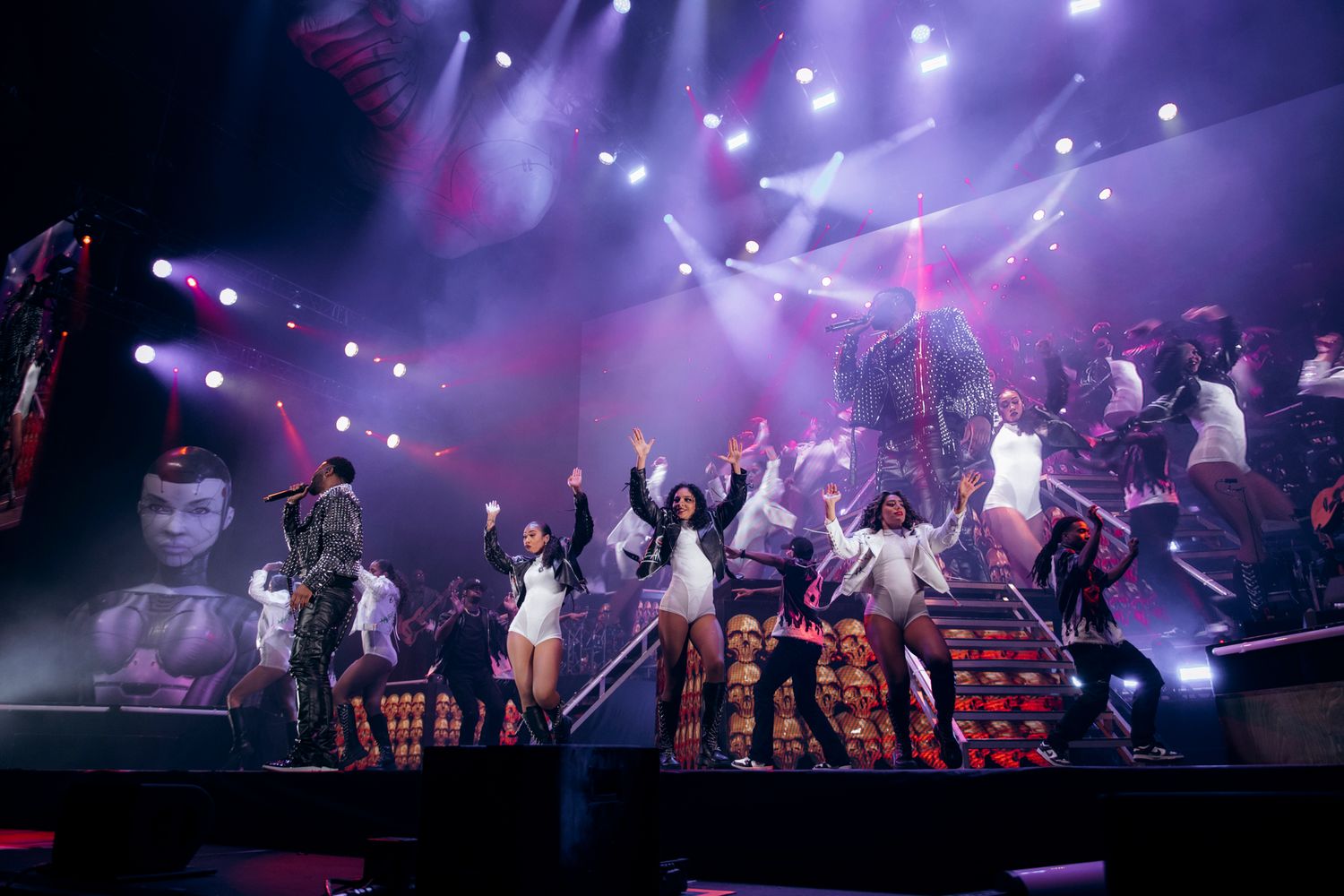 Performers on stage during a concert with dramatic purple lighting and special effects creating an energetic atmosphere.