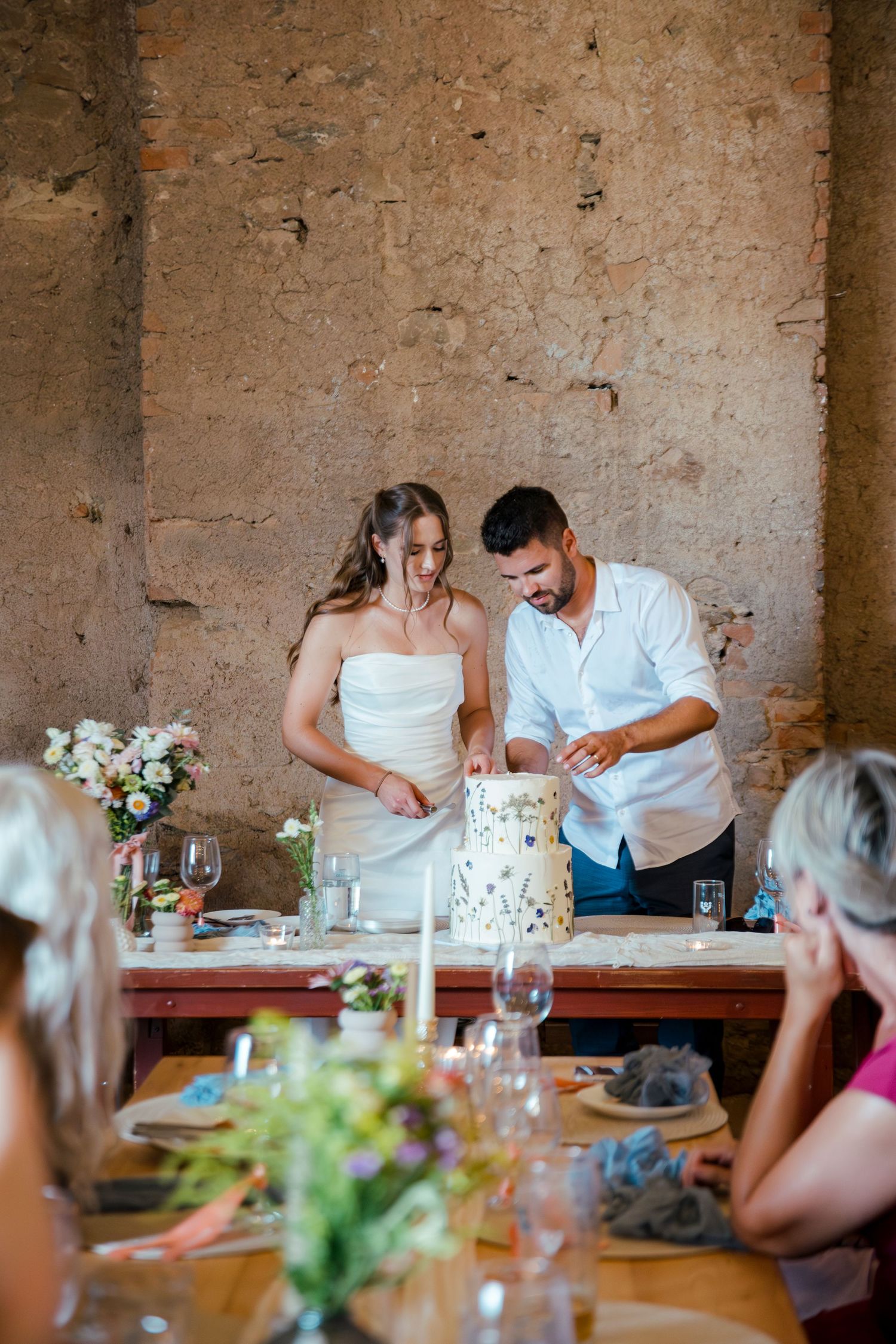 Wedding reception dinner setup in rustic stone venue with elegant table settings.