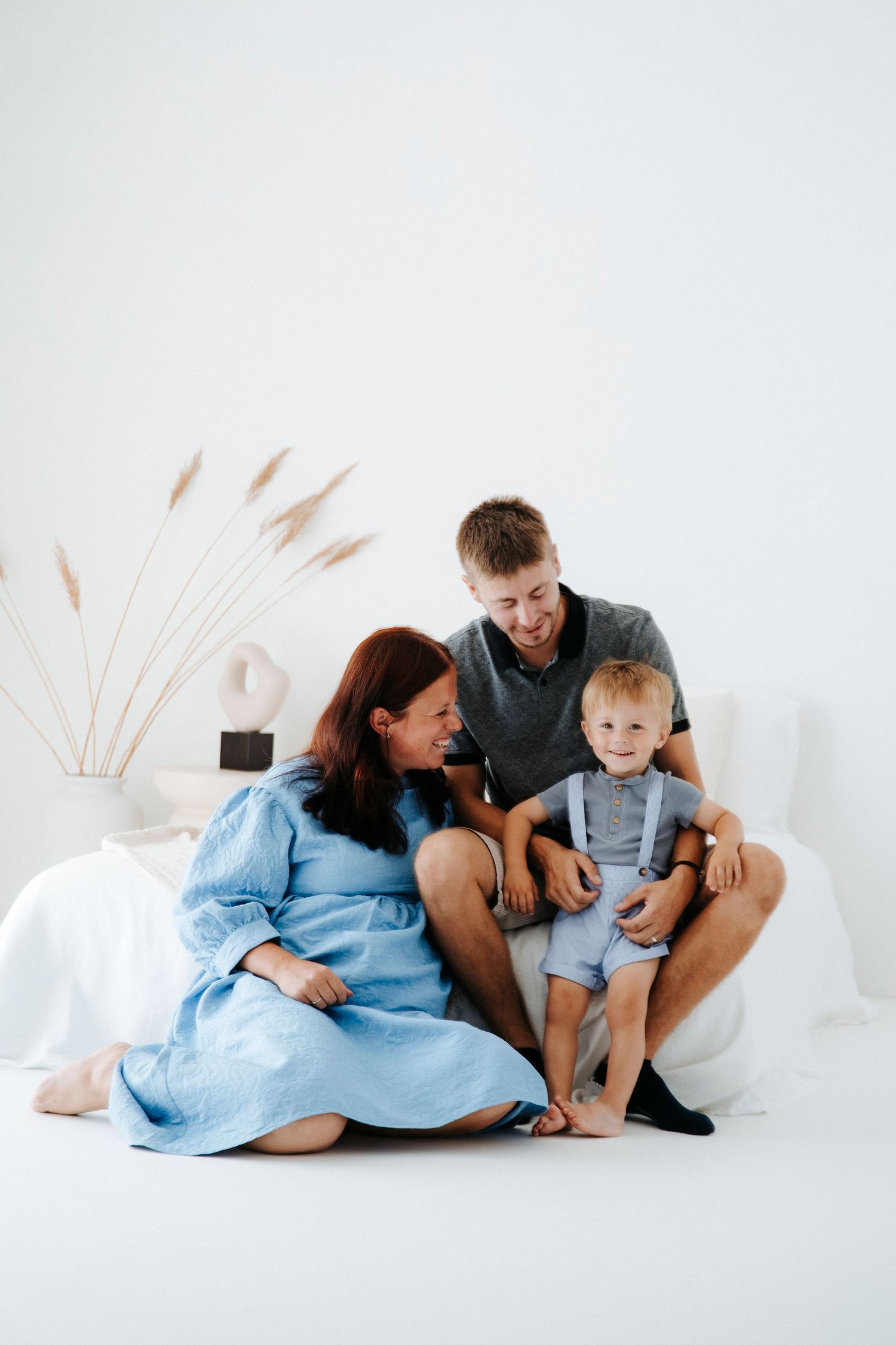 Family in coordinated blue and black outfits poses together on white background with pampas grass.