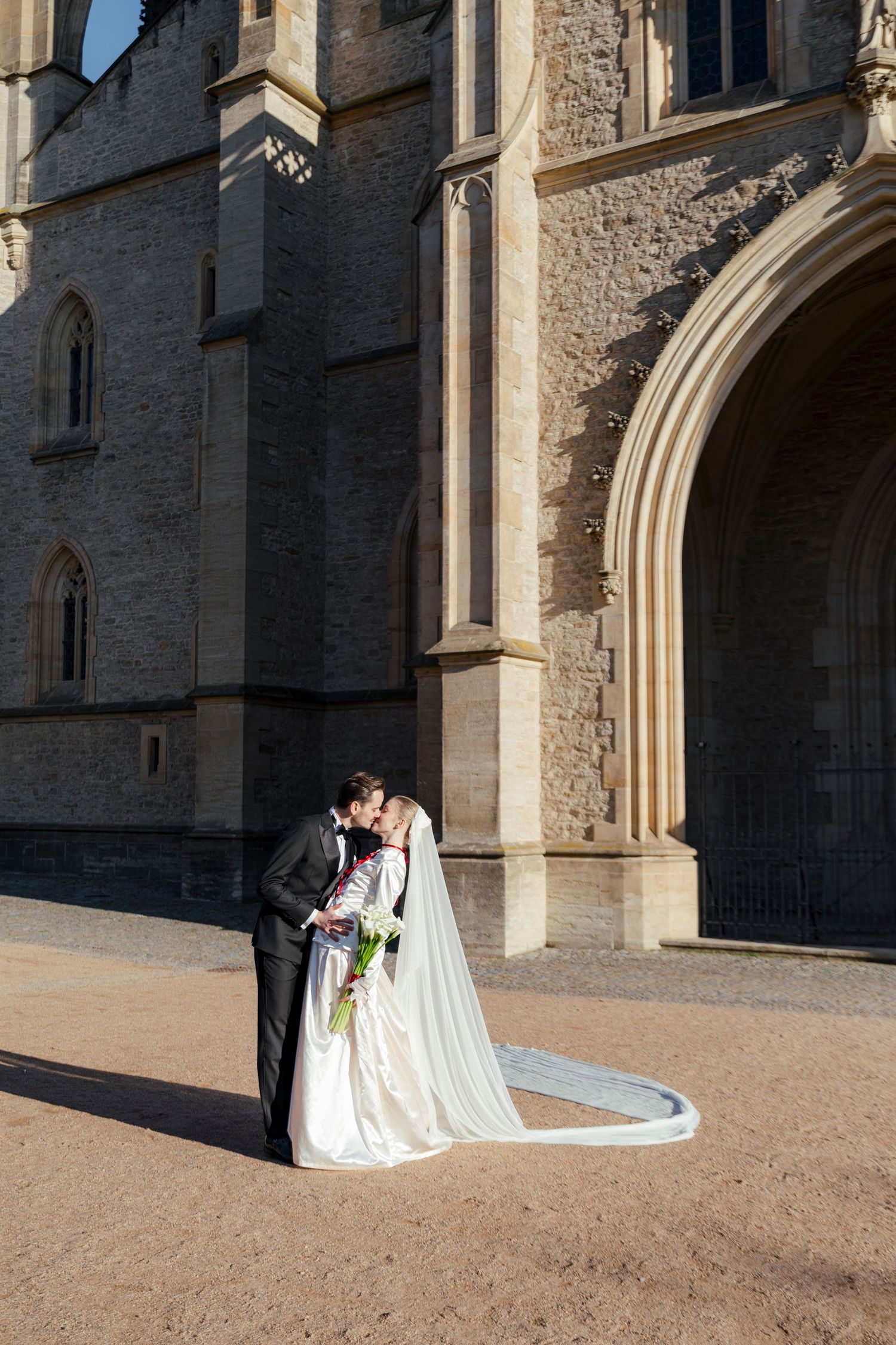 A couple shares a romantic moment outside a gothic stone church on their wedding day.