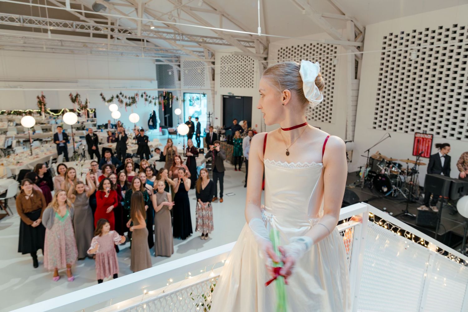 Wedding guests mingle and dance in an elegant white venue with modern decor and string lights.
