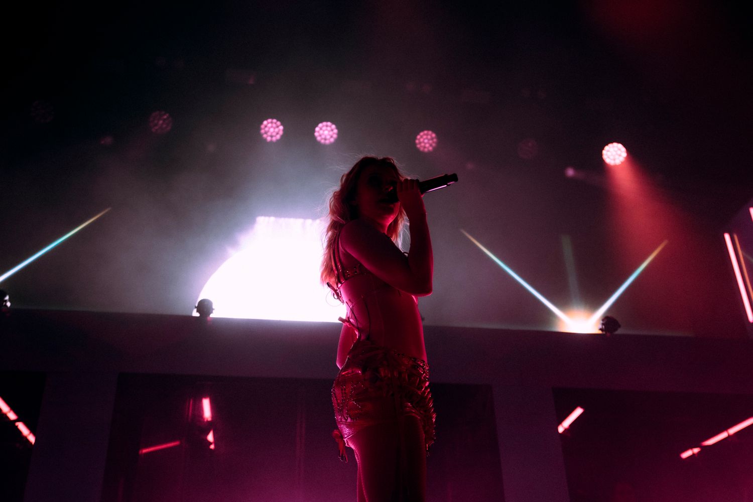 Concert performer silhouetted on stage with dramatic pink and red lighting effects during a live music performance.
