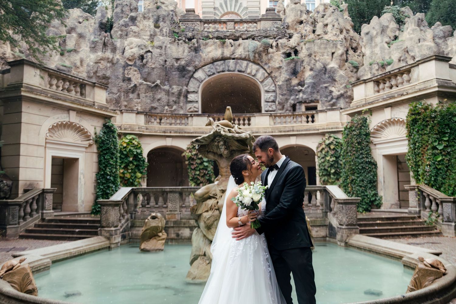 Wedding couple posing in ornate stone courtyard with classical architecture.