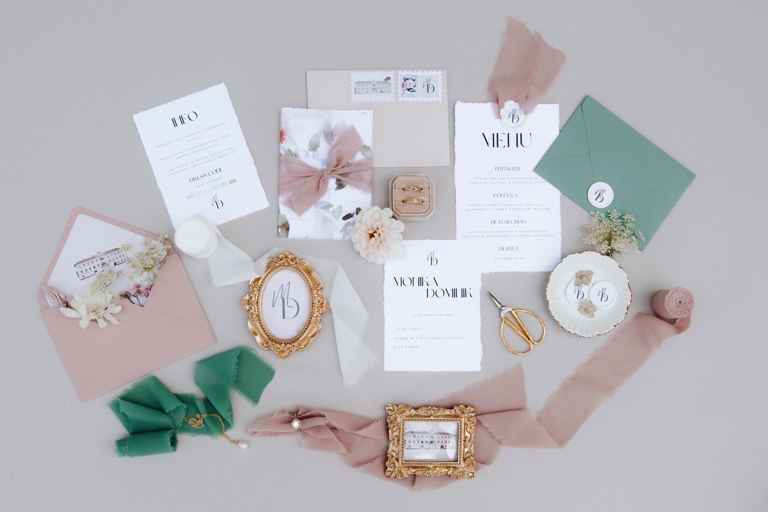 Wedding stationery flatlay featuring pastel pink and green paper elements with floral accents.